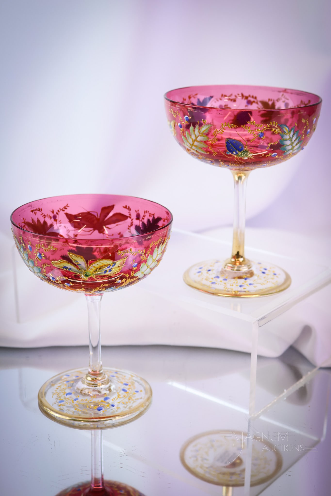 2 pc Lot Moser Cranberry Cocktail Stems Enameled Bugs Flowers & Foliage: A pair of Moser cranberry gilt and enameled glass cocktail stems. Each is lavishly decorated around the bowl with bugs, flowers, and foliage. Each measures 4 1/2" tall. SHIPPING NOTICE: If you choose 