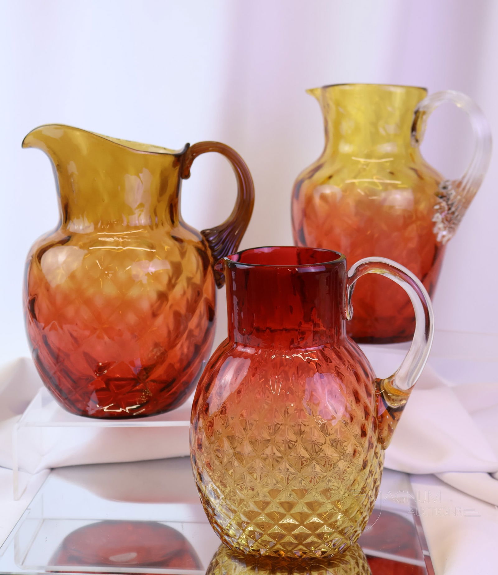 3 pc Lot Victorian Amberina Glass Diamond Quilt Water Pitchers: Three unique finds in Victorian amberina glass water pitchers. There is a square example attributed to Phoenix glass. There are also two reverse amberina examples. The tallest measures 9". SHIPPING NO