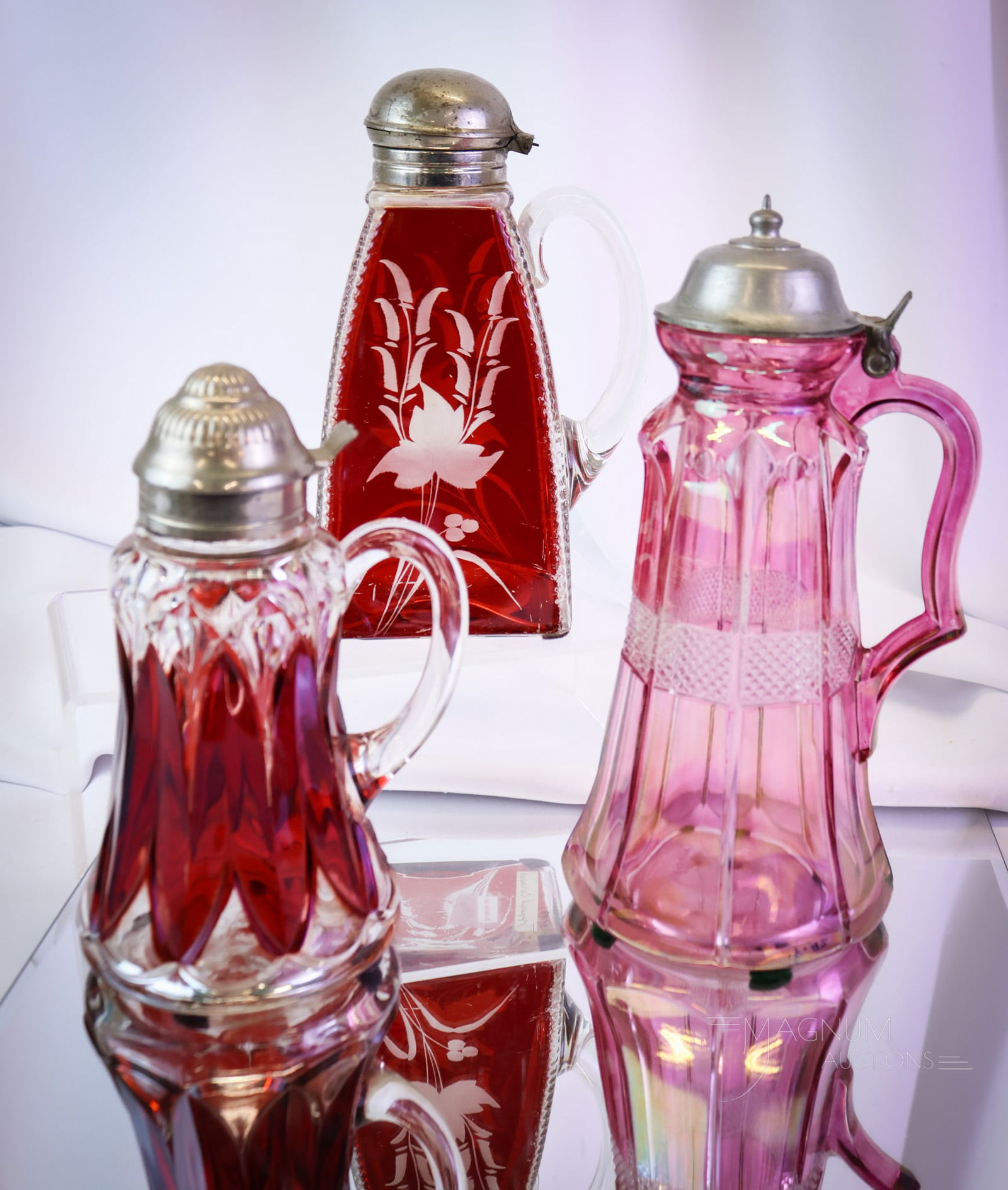 3 pc Lot Victorian Ruby Stained Glass Syrup Pitchers: What a nice lot this is! This lot of three ruby-stained Victorian glass cruets includes some very nice examples. The patterns include Zippered Corners, Arched Ovals, and a Maiden's blush stain Banded