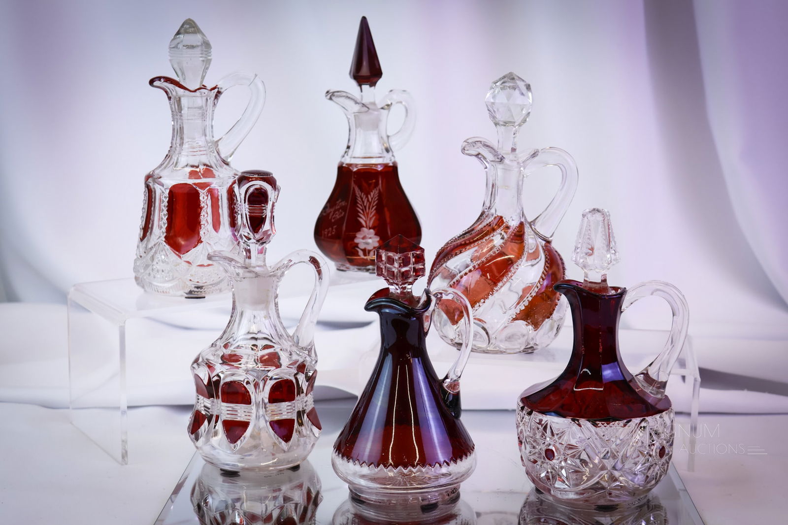 6 pc Lot Victorian Ruby Stained Glass Cruets: Six unique patterns comprise this generous lot of Victorian ruby-stained glass cruets. The lot includes patterns as Hildago, Radiant Daisy, Duncan Ellrose, and more. The tallest measures 7". SHIPPING