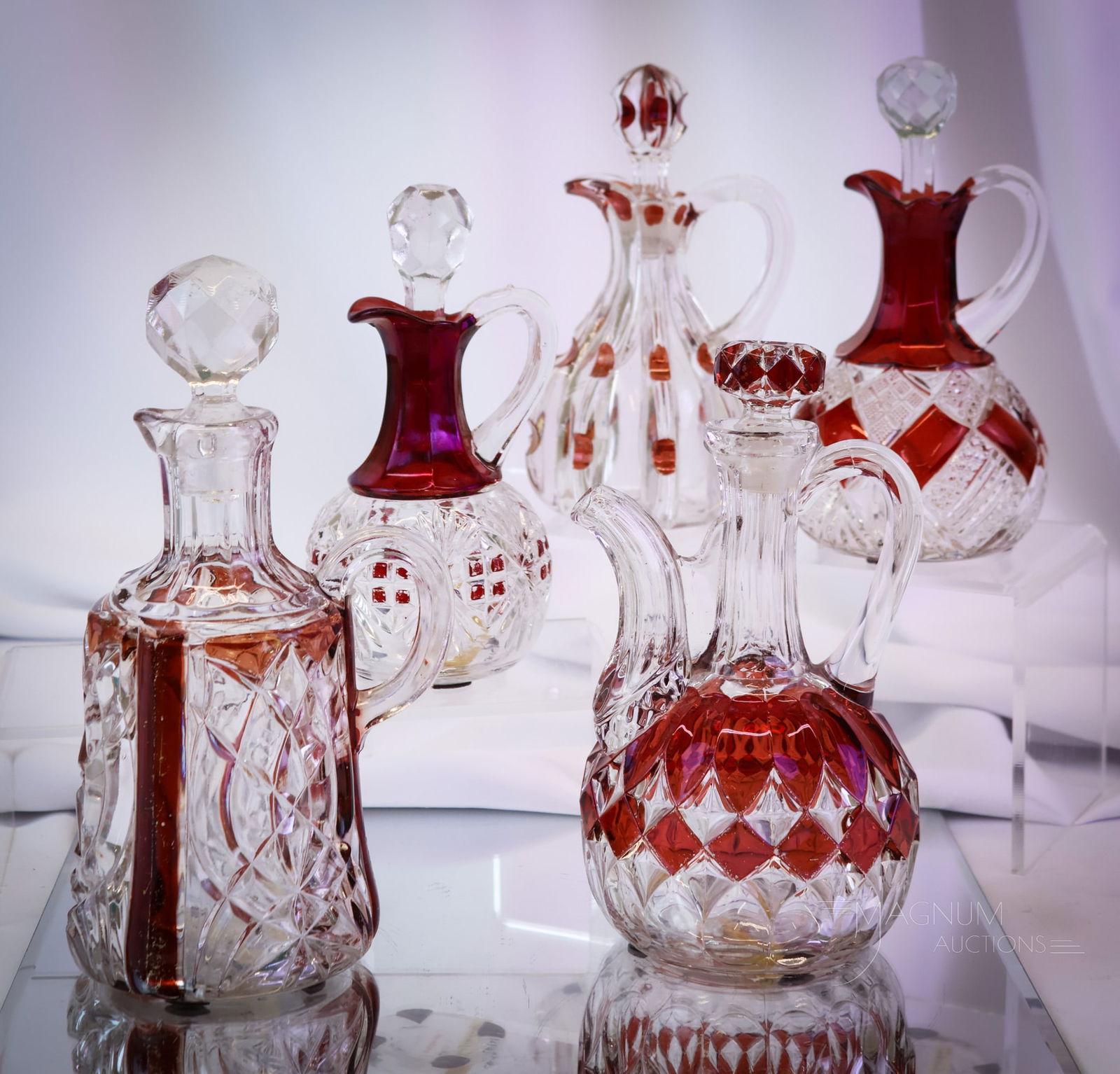 4 pc Lot Victorian Ruby Stained Glass Cruets: Four distinct examples of Victorian glass cruets with ruby stain decoration. The patterns include Wimpole, majestic, Broken Column, Pioneer's Victoria, and National's Eureka. The tallest measures 8 1/