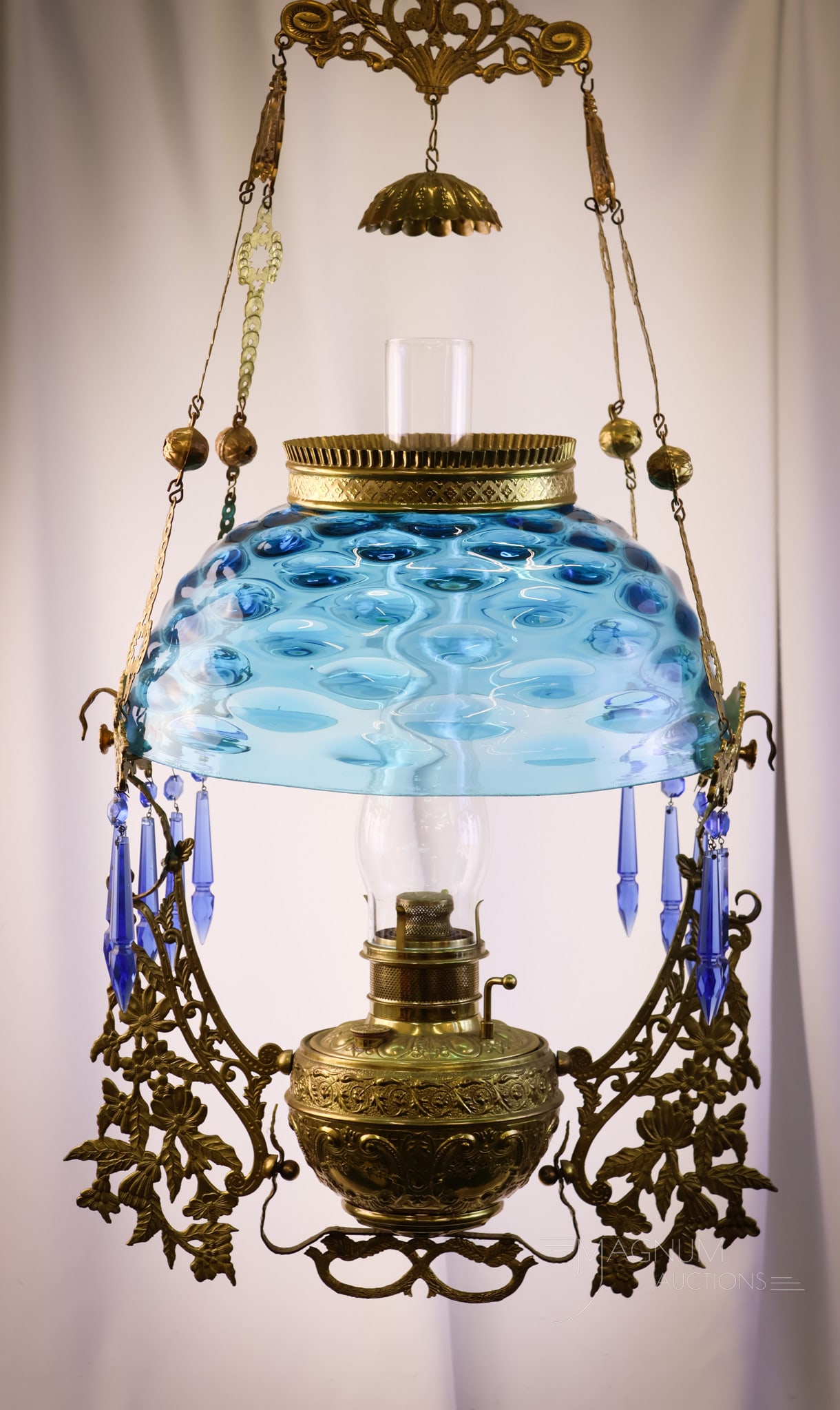 Victorian Blue Glass Bullseye Hanging Parlor Oil Lamp: Here's a fine lamp. This is a brilliant blue Bullseye pattern hanging parlor oil lamp. This lamp is adorned with blue prisms. The frame is bright brass and is ornate with decorative flowers. The lamp