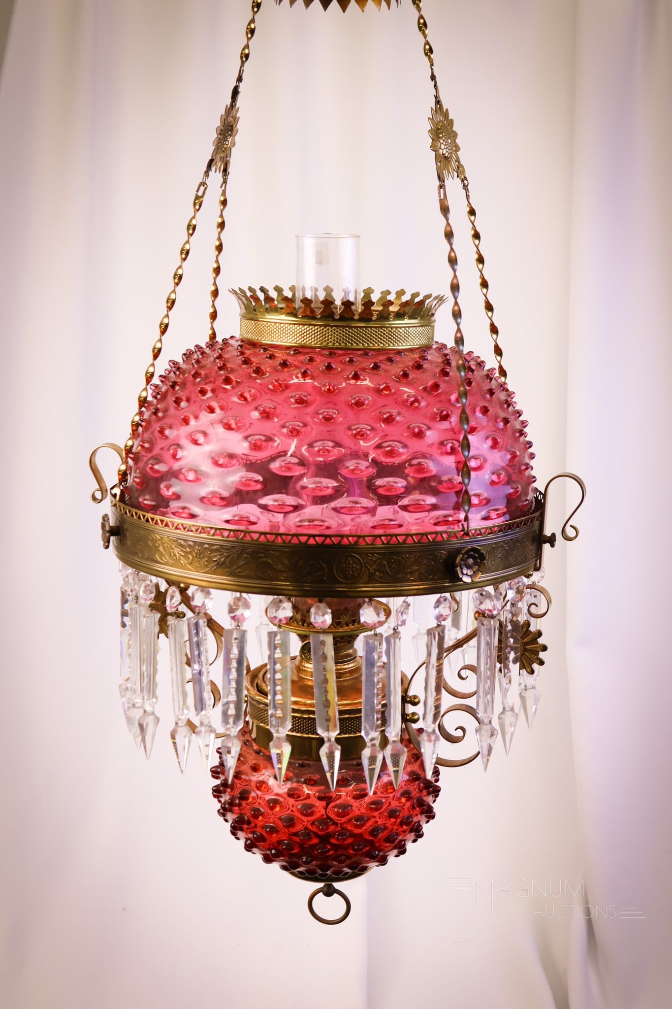 Cranberry Hobnail Victorian Hanging Parlor Oil Lamp: A wonderful, deep cranberry hanging parlor lamp with a matching font in a Hobnail pattern. This lamp burner is marked Solar Em. Co. The frame has sunflowers. The lamp is completed by large cut prisms.