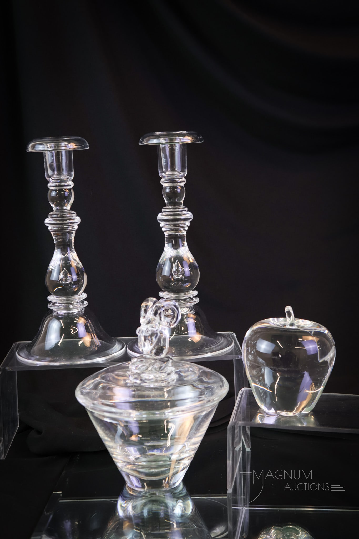 4 pc Lot Crystal Steuben Candlesticks & More: A nice find in crystal Steuben art glass. This lot offers a pair of baluster-form controlled bubble candlesticks. These, along with an apple paperweight. The last piece is a ram's head covered candy d