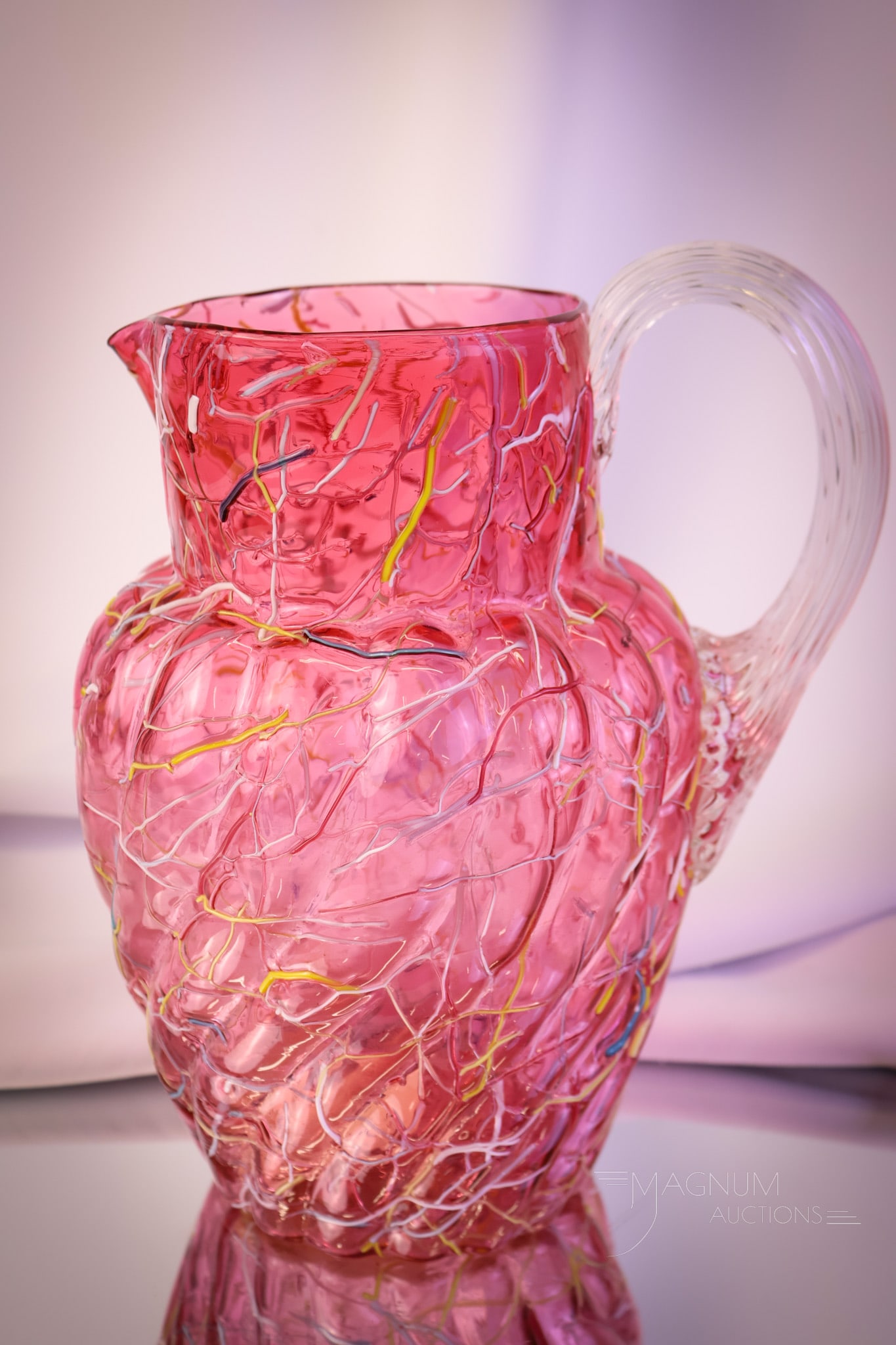 Phoenix Victorian Cranberry Peloton Art Glass Water Pitcher: A beautiful find in a Victorian water pitcher. This pitcher is in the swirl mold. It is attributed to Phoenix glass. The body is a deep cranberry color glass with rainbow threading around the pitcher.
