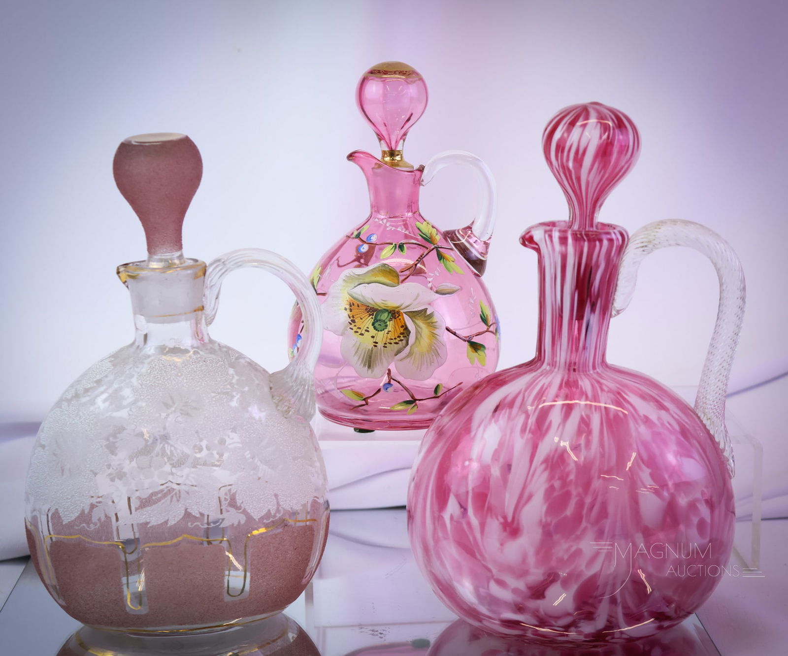 3 pc Lot Victorian Art Glass Claret Decanters: Three unique examples of Victorian art glass claret decanters. The first is a pink and white spatter example. The second is clear with enameled overshot decoration. The third is a cranberry claret wit