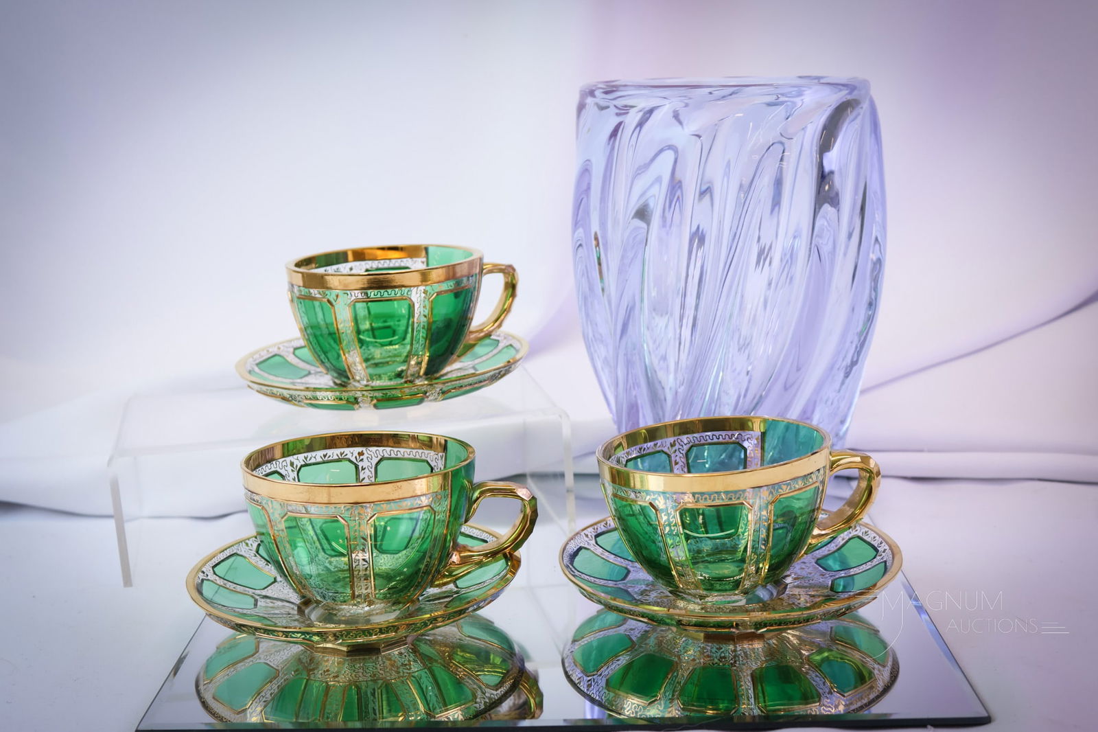 7 pc Lot Bohemian Victorian Art Glass Moser & More: A select offering of a set of three Moser cabochon gilt decorated cups and saucers. These are in clear with green and gold applied cabochons. The seventh piece is an Alexandrite heavy swirl vase. The