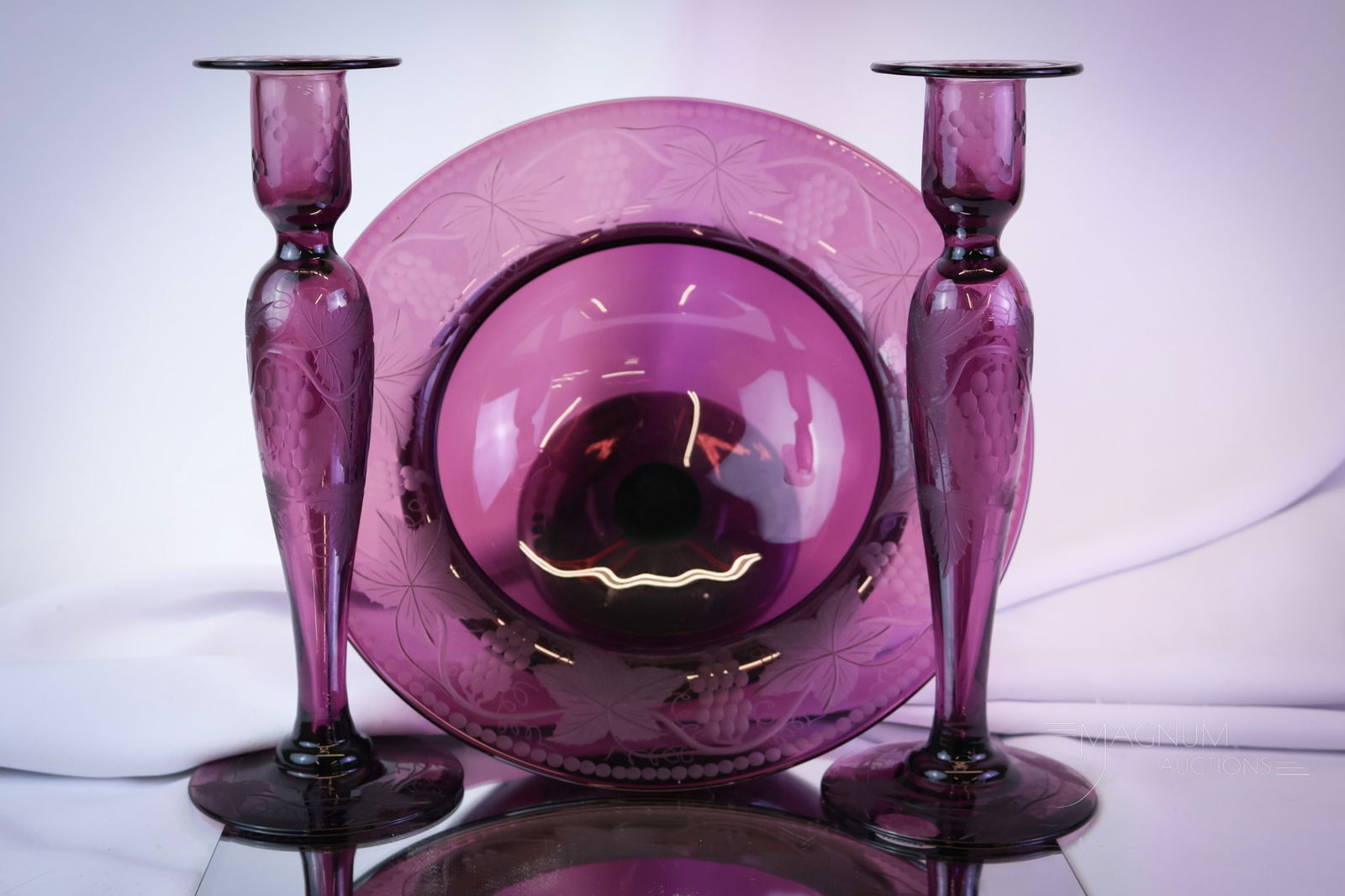 3 pc Pairpoint Grapes Etched Glass Console Set: A wonderful find in Pairpoint glass. This is a console set featuring amethyst glass with grape etching. The set consists of a console bowl and two candlesticks. The tallest measures 10 1/2" tall. SHIP