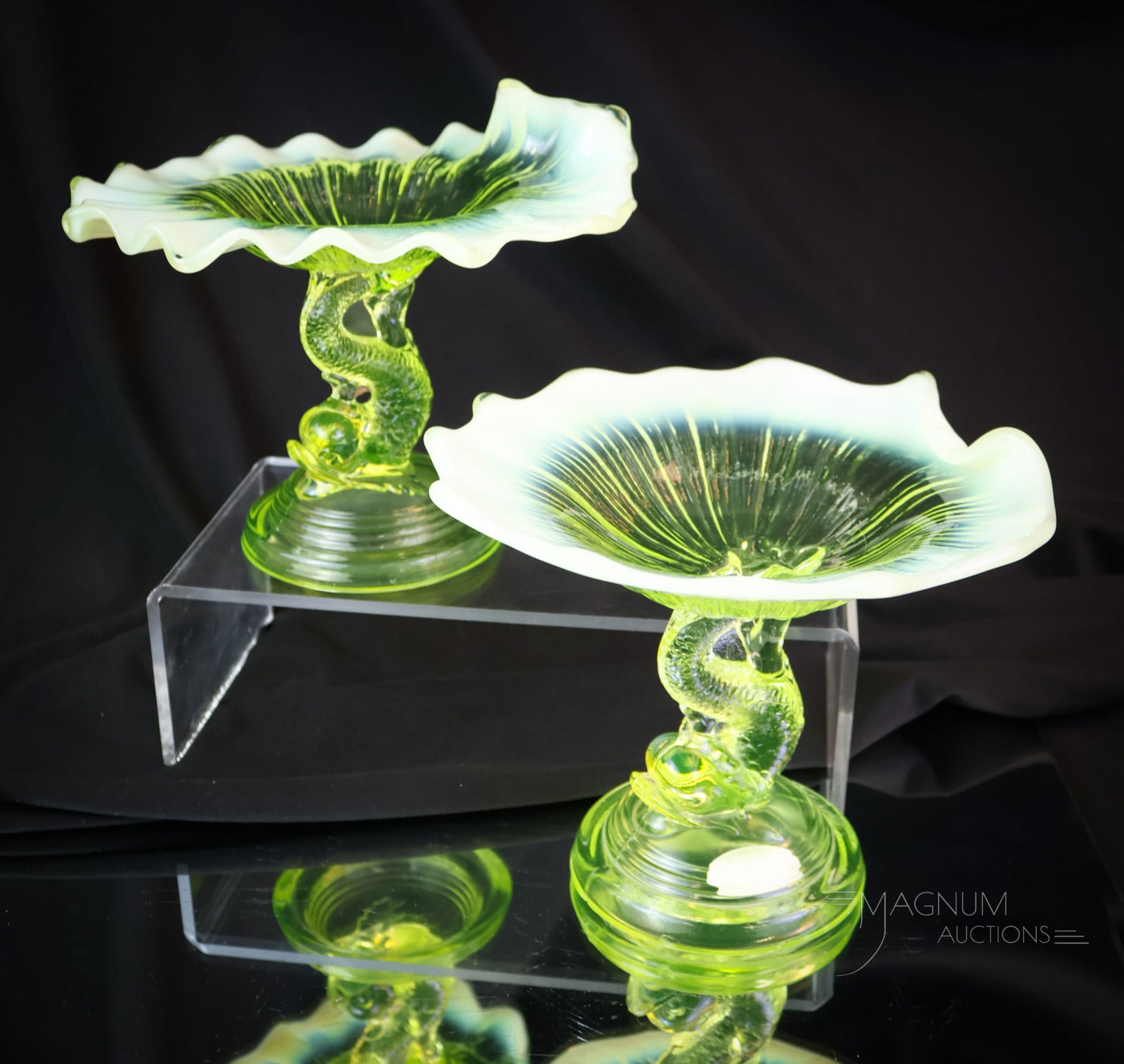 2 pc Lot Vaseline Opalescent Petticoat Dolphin Compotes: Two desirable pieces of uranium-rich vaseline glass. This lot offers two examples of the Petticoat Dolphin compote. Each measures 5 1/4" tall. One example exhibits a chip on the foot rim. SHIPPING NOT