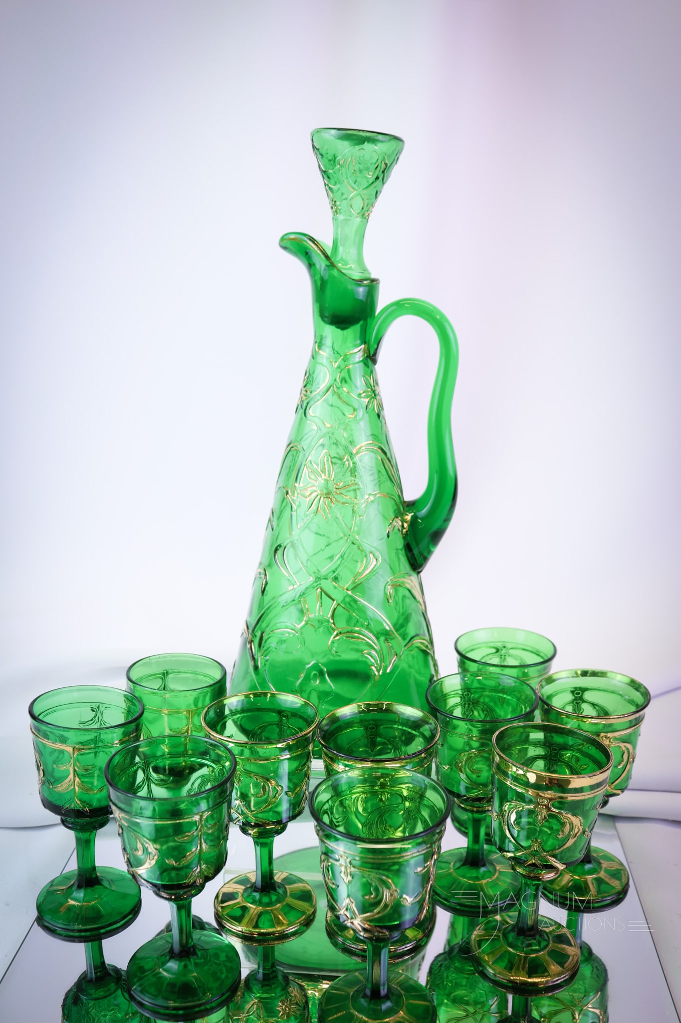11 pc Dugan Victorian Glass Claret Decanter Set: A wonderful cind in a Dugan Victorian emerald green gilt decorated decanter set. This set is a hard-to-find collectible. Not many around, we dare say. The claret retains the original stopper as well.
