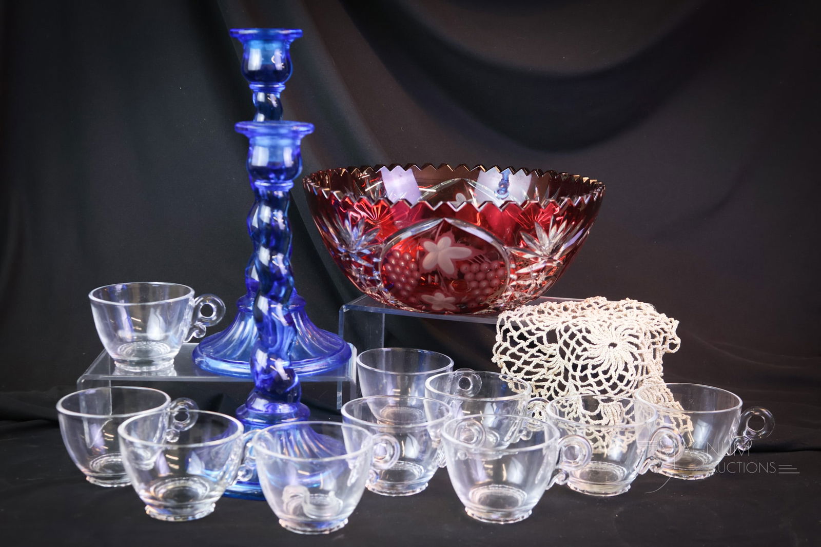 13 pc Lot Collectible Glass Heisey & More: Thirteen-piece lot of collectible glass. This offering includes a contemporary ruby cut-to-clear glass bowl. A set of ten Heisey Lariat punch cups. A pair of blue twist candlesticks. There is also a