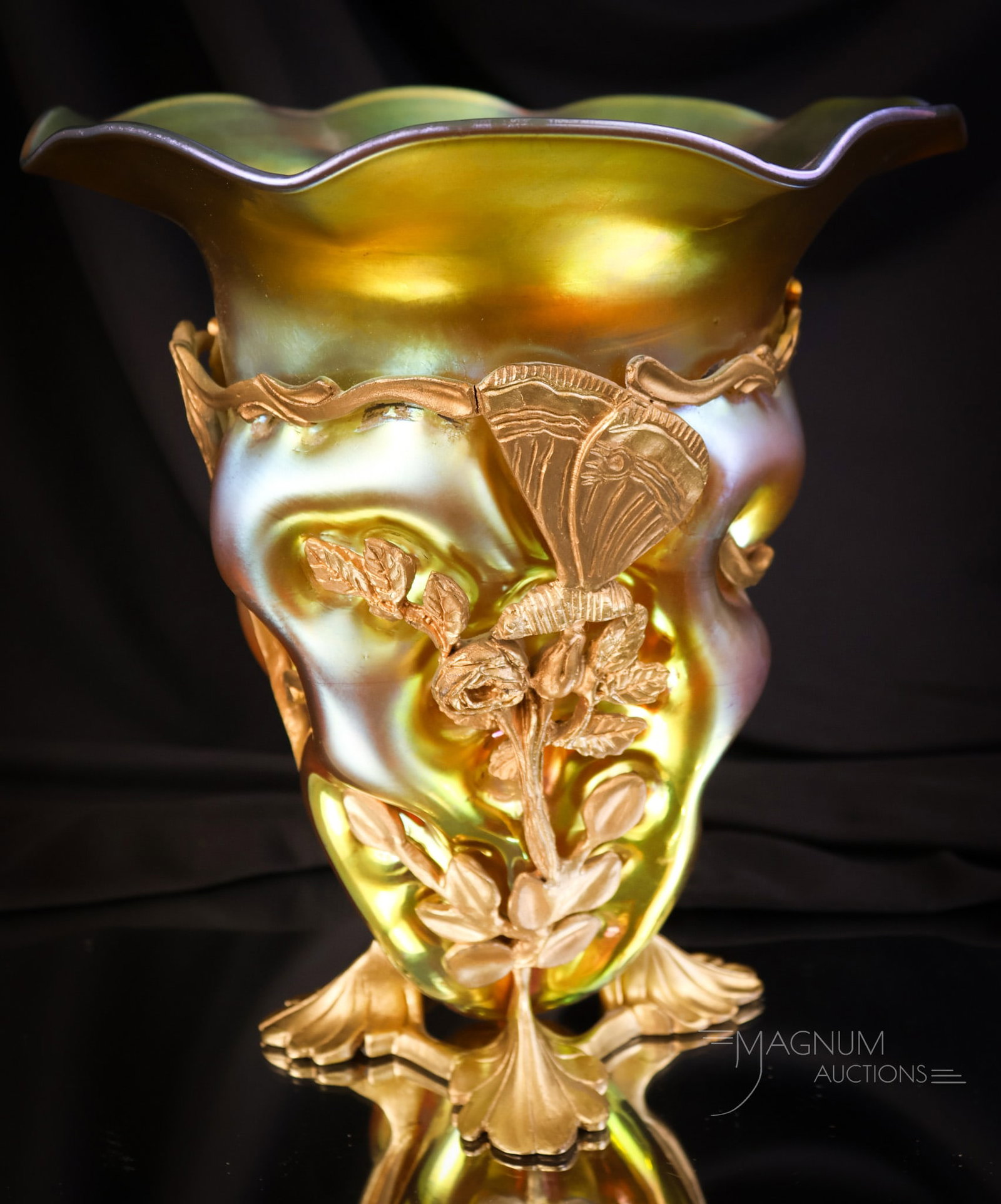 Signed "L.C.T Tiffany Favrile" Gold Blown Out Art Glass Vase in Ormolu Frame: A beautiful find in a brilliant gold iridescent vase. This piece is signed, "L.C.T. Tiffany Favrile." The vase features a blown out design in a gilt ormolu metal cage with butterflies. The vase measur
