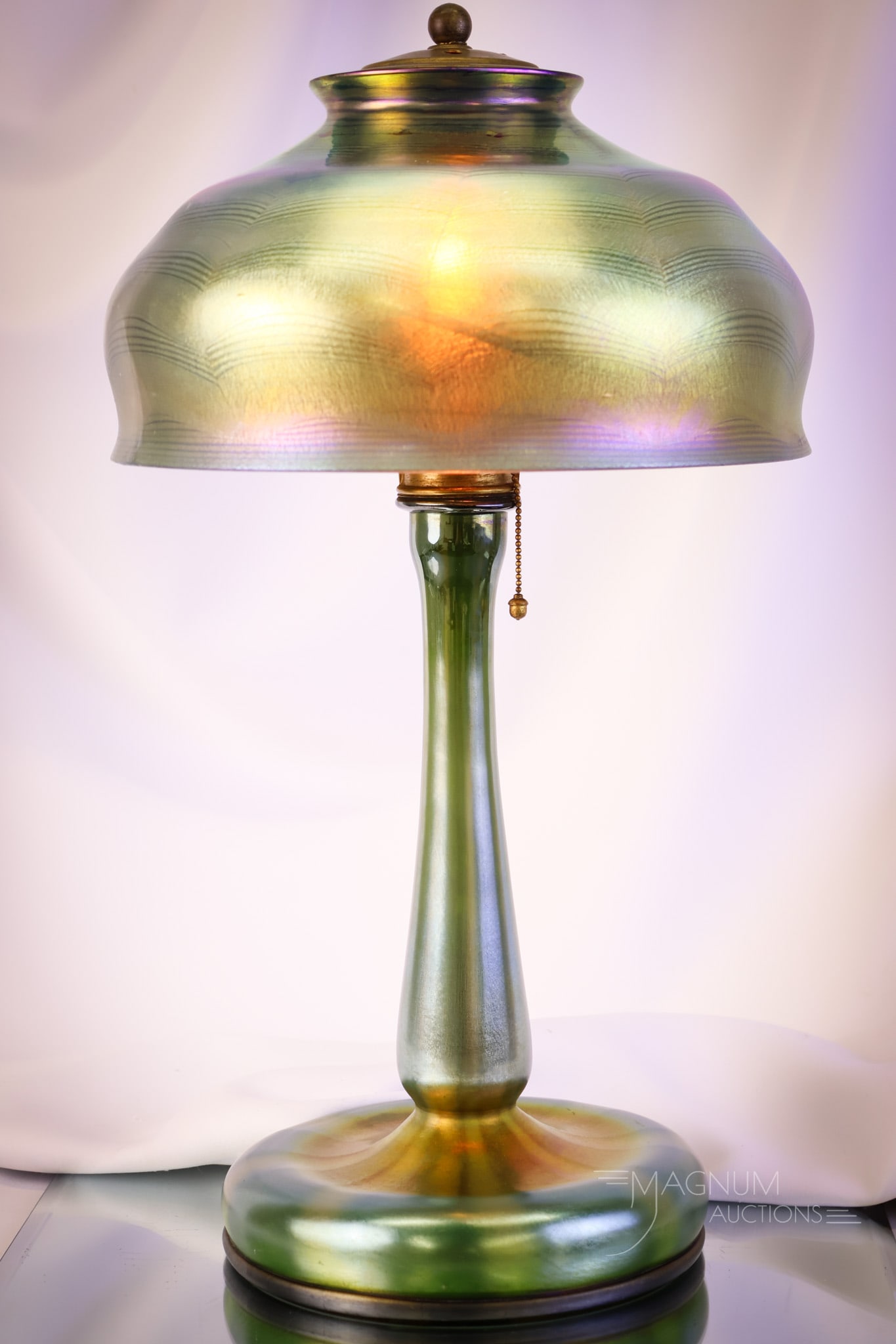 Signed "L.C.T. Tiffany Favirle" Blue Green Iridescent Glass Table Lamp: A beautiful signed Tiffany table lamp. The base is signed, "L.C.T. Tiffany Favrile." The base retains the original harp and mounting. The shade, alas, has been damaged and repaired. It is marked "G21 