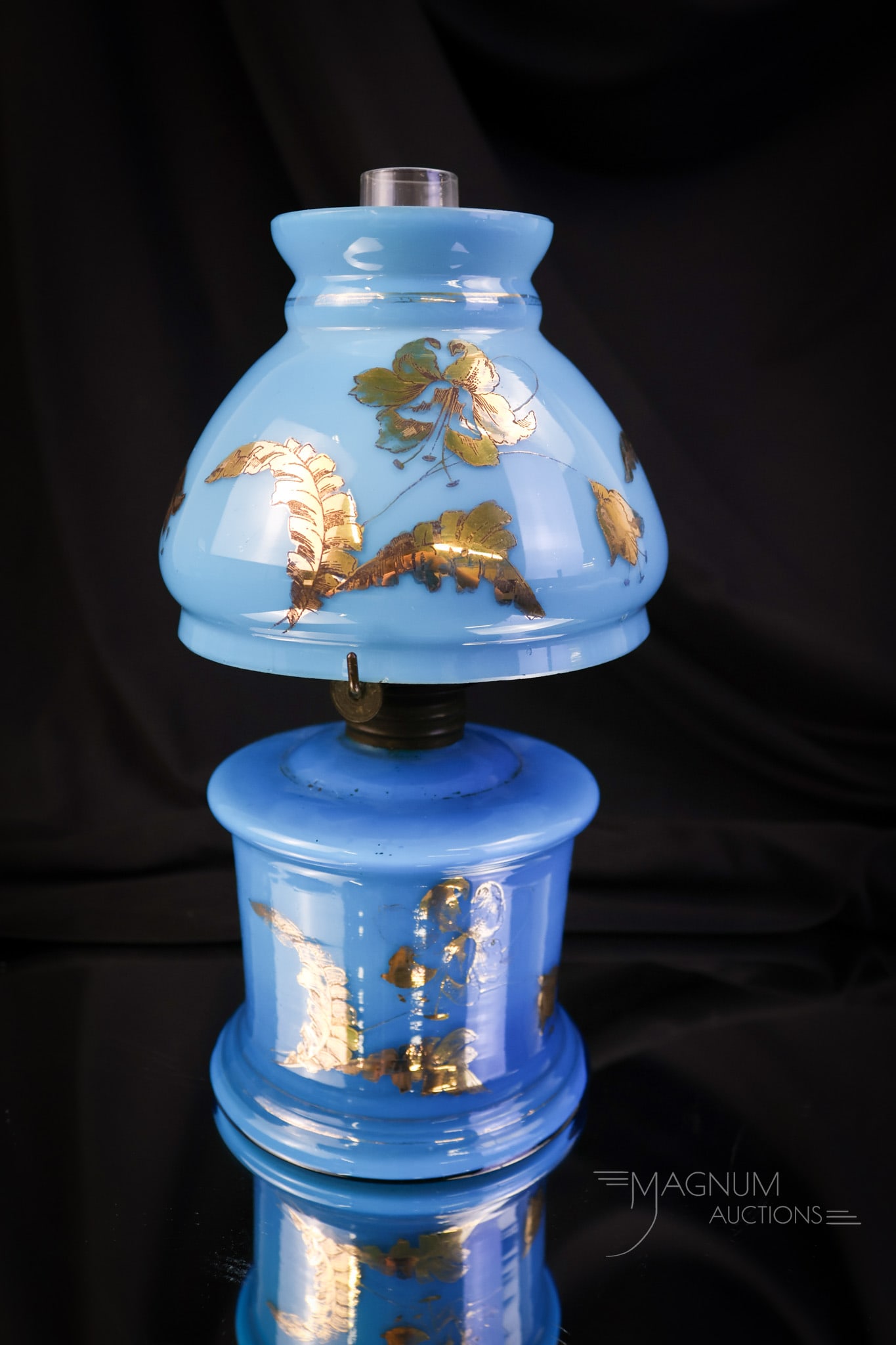 Victorian Blue cased Gilt Decorated Art Glass Miniature Oil Lamp: A beautiful little gilt decorated miniature oil lamp. This lamp is in a deep blue cased glass. The shade and the base are gilt decorated with flowers. The lamp measures 8" tall and 3 3/4" wide. SHIPPI