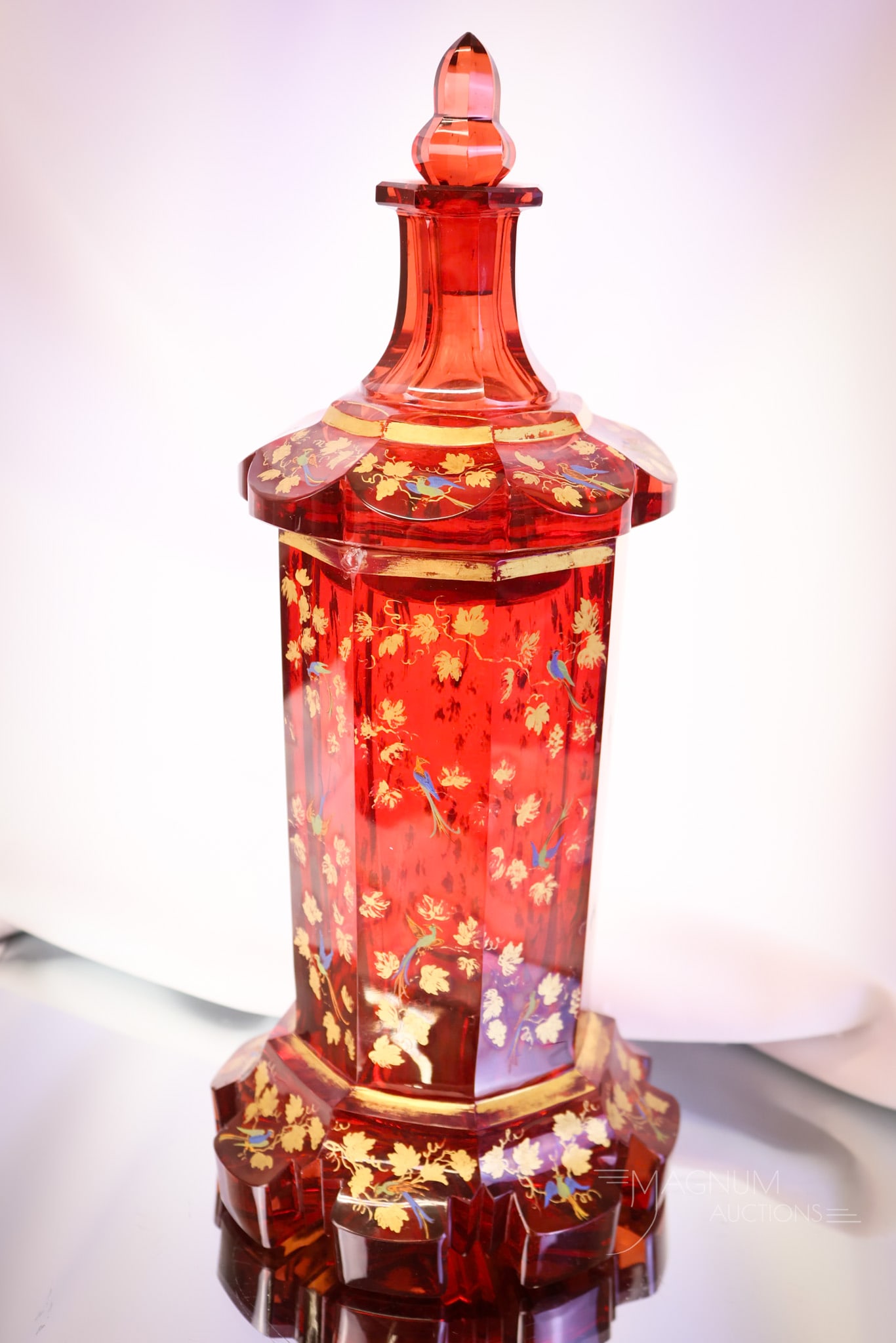 Bohemian Ruby Gold Enameled Biedermier Cut Covered Jar: A beautiful Bohemian cut glass jar in ruby with gold enameled and bluebirds. The piece has Biedermeier-style cut designs. The jar measures 12" tall and 5" wide. A chip is noted near the base rim. SHIP