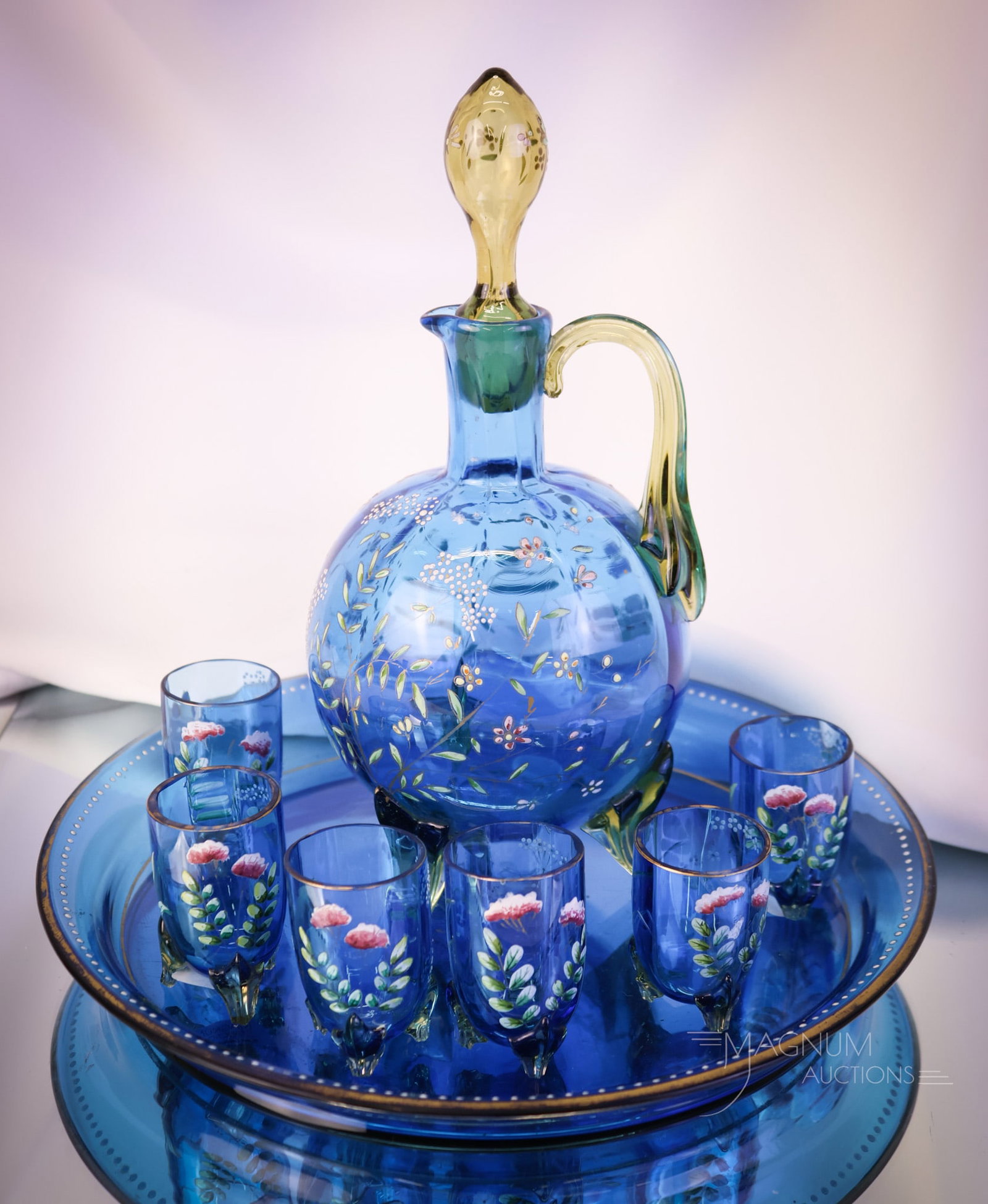 8 pc Moser Prussian Blue Enameled Gilt Decorated Glass Liquor Set: A select offering of a Moser Prussian blue enamel and gilt decorated Liquor set. This set has amber applied handles, a decanter stopper, and cordial feet. The tallest of the set measures 9" . SHIPPING