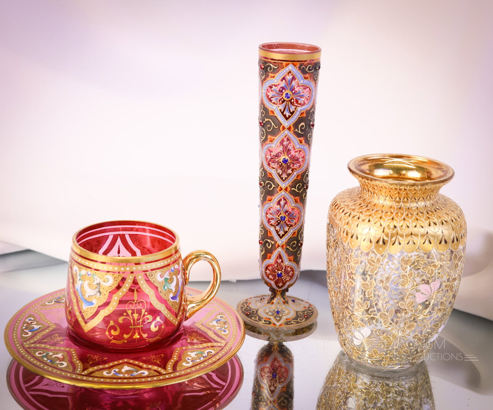 4 pc Lot Moser Cranberry Gilt Enameled Art Glass: Four delights in Moser cranberry gilt and enamel decorated glass. This lot offers a cup and saucer. A pinched vase with all-over gold enamel decoration. Lastly, a cranberry bud vase with fine enamelin