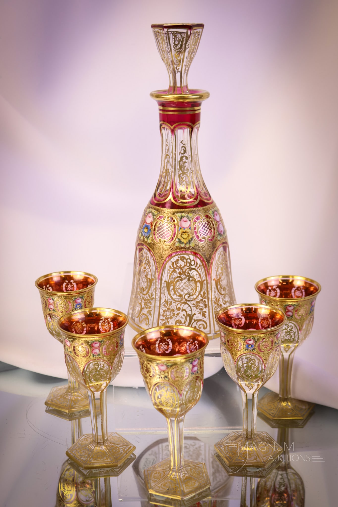 6 pc Moser Cranberry & Clear Gilt Enameled Decanter & Glasses: A beautiful six-piece Moser cranberry and clear glass, finely gilt and enamel-decorated decanter set. This offering includes the decanter and five glasses. The tallest measures 5". SHIPPING NOTICE: If