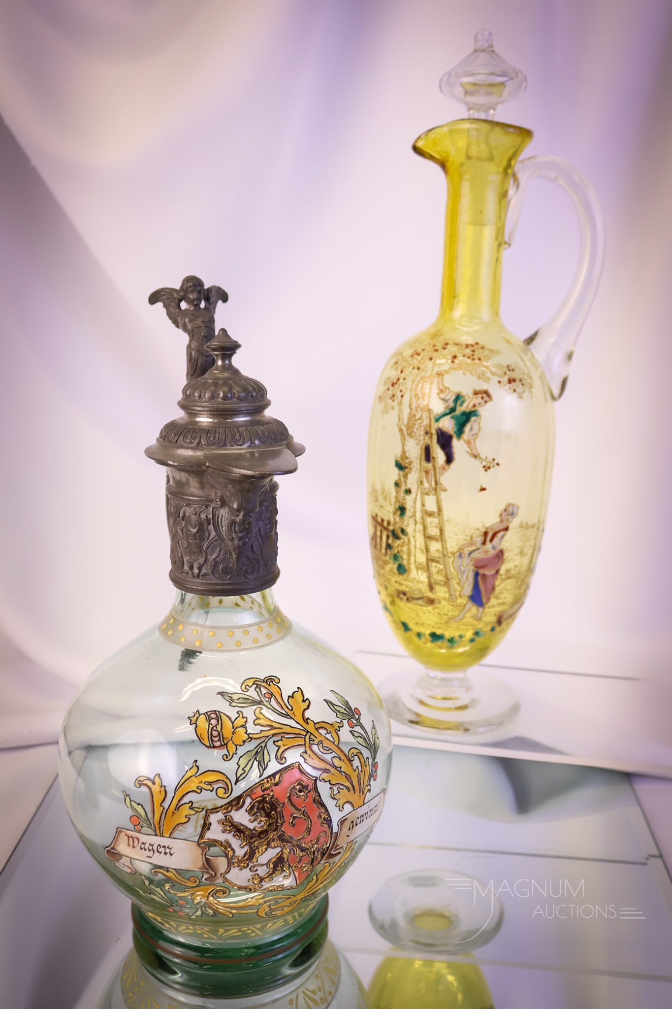 2 pc Lot Enameled Antique Glass Vessels German & Rossler Clarets: Two unique finds in antique art glass clarets. The first is a German piece with a figural pewter spout and handle of a winged lady. Ths second is a tall example enameled by Rossler featuring a couple 