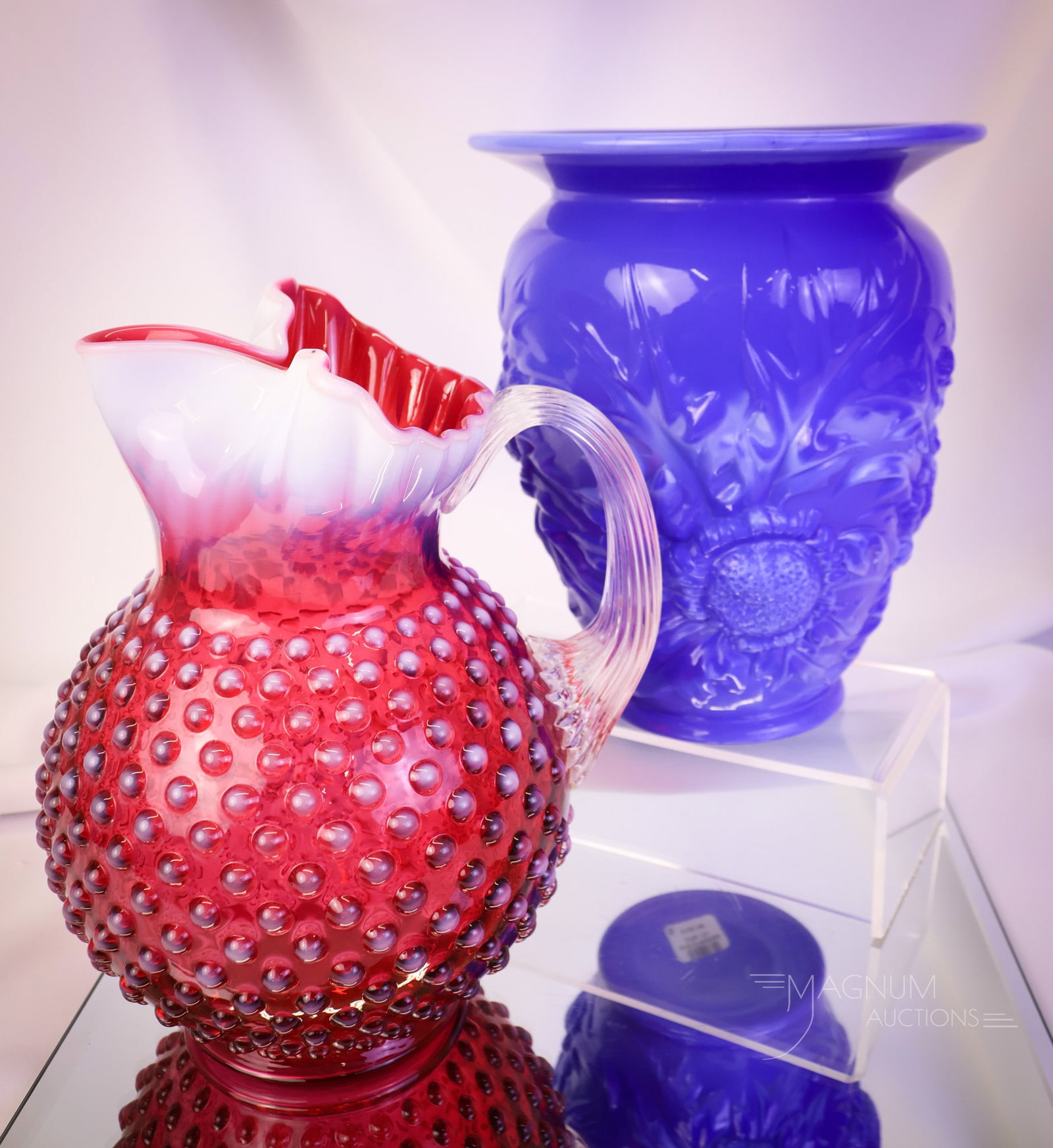 2 pc Lot Fenton Opalescent & More Art Glass: Two distinct finds in Fenton art glass. The first is a cranberry opalescent hobnail pattern ice-lip pitcher. The second is a Periwinkle blue Thistle vase. The tallest measures 9". SHIPPING NOTICE: If 
