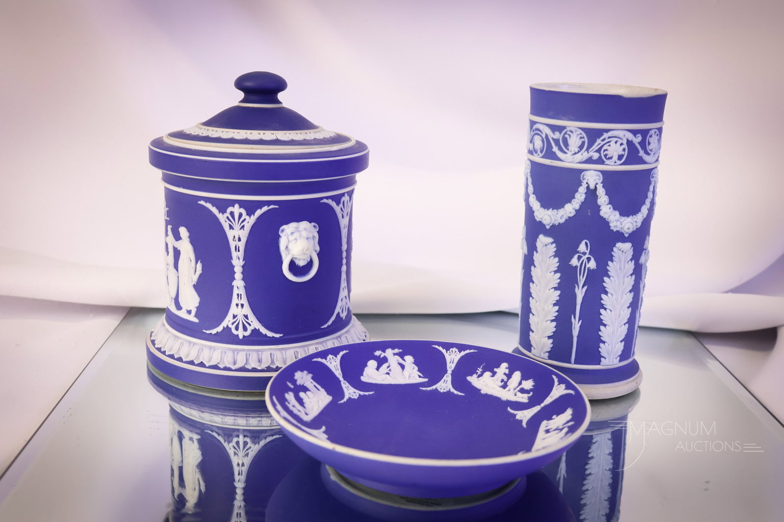 3 pc Marked Wedgwood Blue Jasperware: Three selections in marked Wedgwood blue Jasperware. This lot offers a cylindrical vase, a small plate, and lastly, a lidded humidor. The tallest measures 5 1/2". The lid has a tiny rim chip The base 