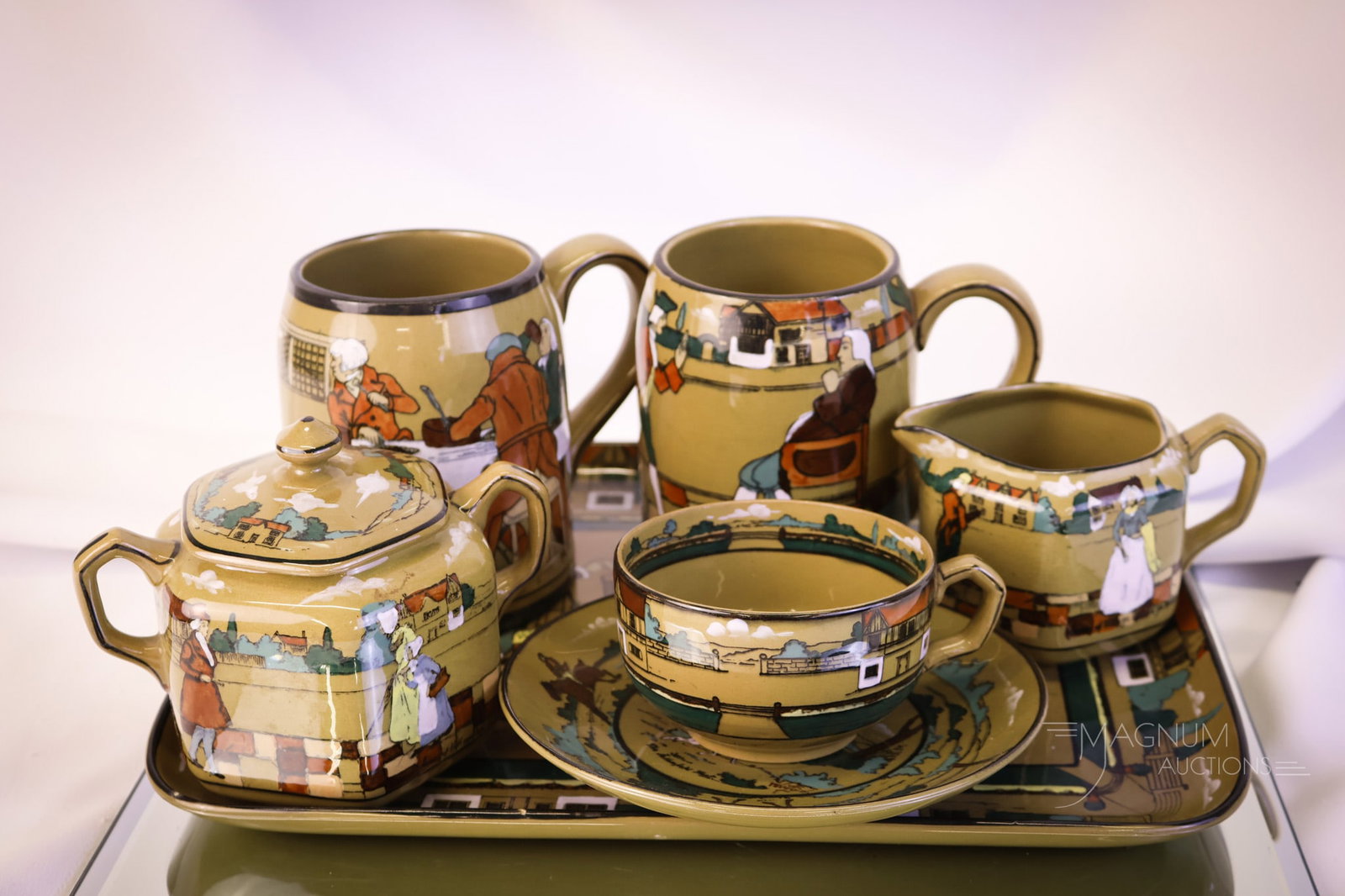 7 pc Lot Buffalo Deldare Pottery: A generous assortment of Buffalo Deldare pottery. The lot includes a tray, two mugs, a creamer, a covered sugar, and cups and saucers. The tallest measures 4 1/2". SHIPPING NOTICE: If you choose not t