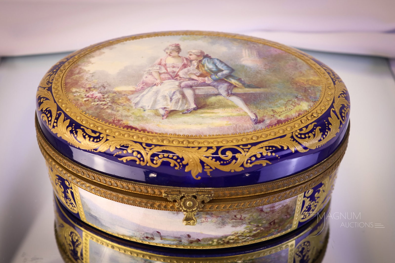 Sevres Cobalt & Gold Decorated Oval Hinged Dresser Box: A fine piece of Sevres cobalt and gold porcelain. This is an oval dresser box featuring a courting scene on the lid and a forest scene on the front side. The box measures 2 1/2" tall and 7 1/2" wide. 