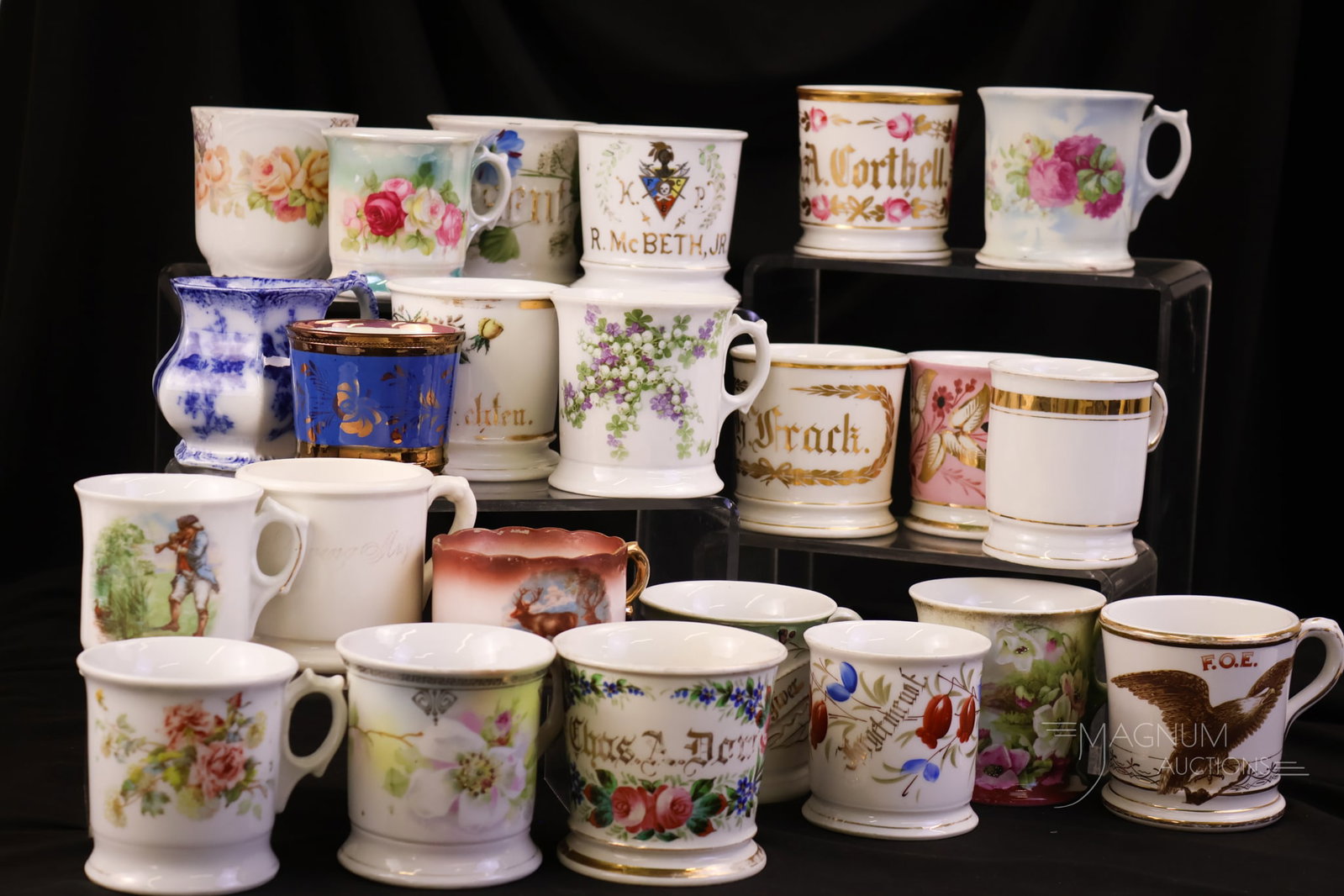 23 pc Lot Victorian Shaving Mugs: A generous offering of twenty-three Victorian shaving mugs. Various examples in the lot. There are Flow Blue, Fraternal, Names, and floral-decorated mugs. The tallest measures 3 3/4".