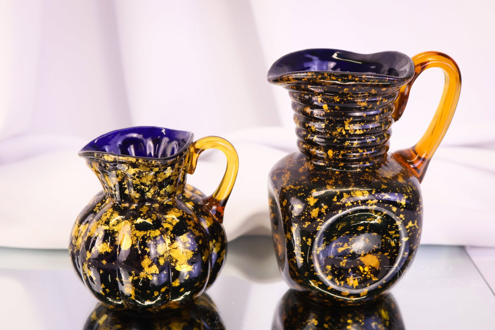 2 pc Lot Hobbs Cobalt Victorian Spangle Glass Cream Pitchers: Two unique finds in Hobbs cobalt spangle glass. Both are in cobalt with gold flakes and amber applied glass handles. The tallest measures 5".