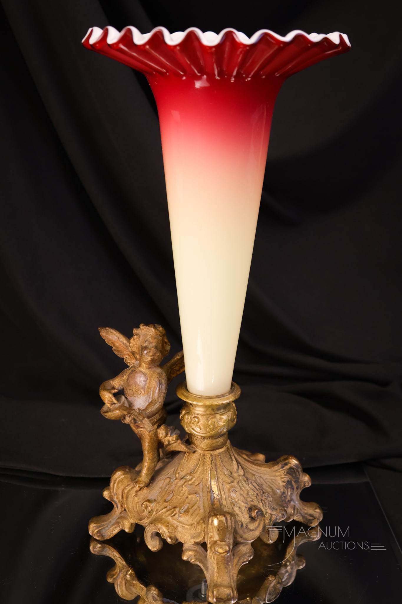 Peachblow Uranium Art Glass Lily Vase in Cherub Holder: A fine uranium-rich peachblow art glass lily vase set in a figural cherub adorned gold-toned holder. This vase lights up under black light. The piece measures 11 1/4" tall.