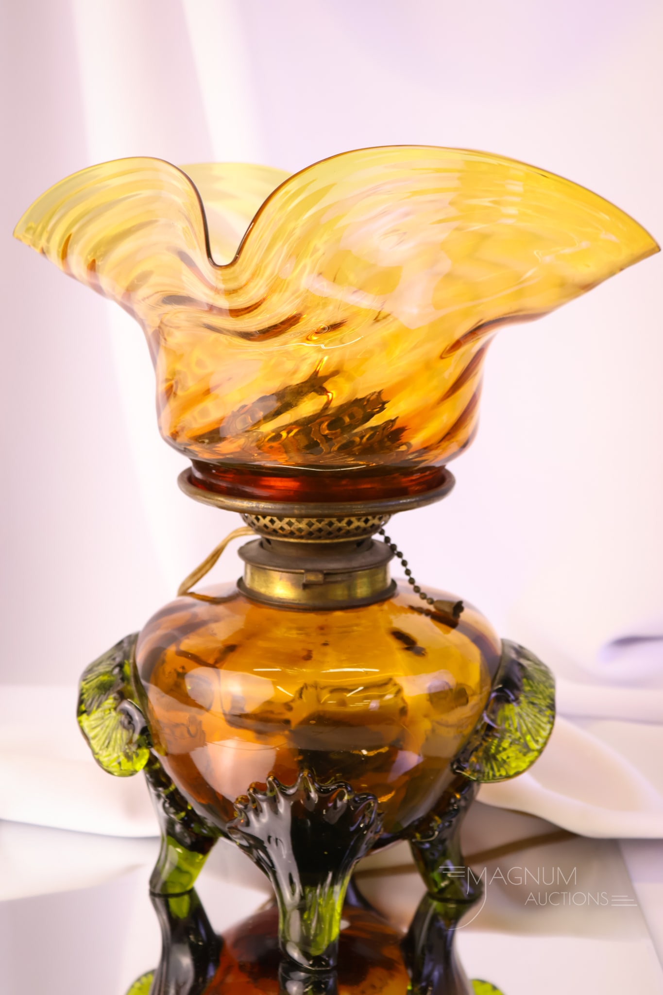 Victorian Amber Art Applied Glass Oil Lamp: An unusually beautiful applied art glass oil lamp. This lamp is in a rich honey amber with applied green leaf-form handles and tendril legs. The burner has been electrified. The lamp measures 12 1/2" 