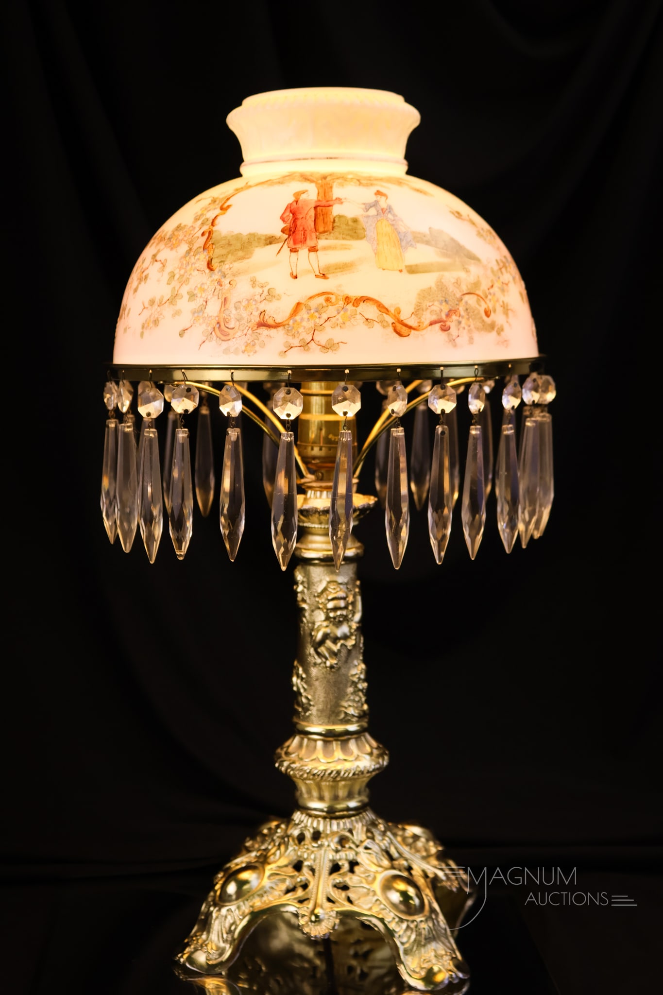 Wave Crest Glass Cheub Adorned Table Lamp: A beautiful Victorian table lamp. The shade is attributed to Wave Crest. It features a courting scene. The base is gilt with an embossed cherub design. Prisms circle the shade ring. The lamp measures 