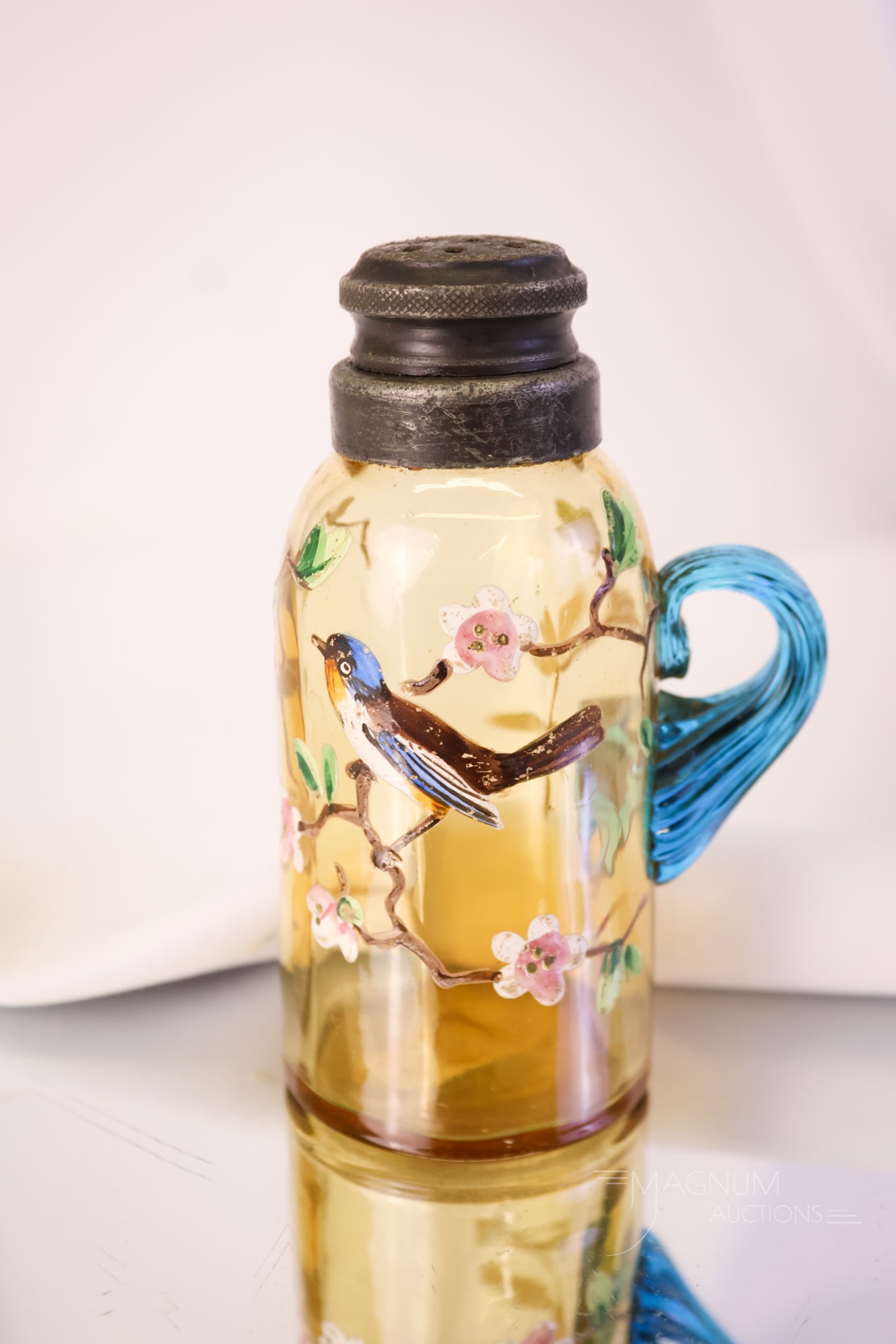 Rare Handled Victorian Enameled Glass Salt Shaker: A rare shaker, folks! This shaker features an amber body with an applied blue glass handle. The shaker is decorated with a flowering branch and a bird. The shaker measures 4 1/4" tall.