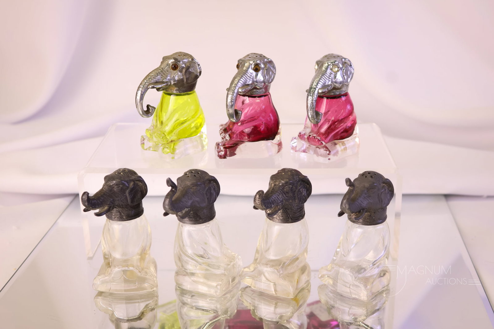 7 pc Lot Antique Figural Glass Elephant Salt Shakers: A seven-piece lot of antique figural glass elephant salt shakers. There are four clear, a pair of ruby, and a citron. Each measures 2 1/2" tall.
