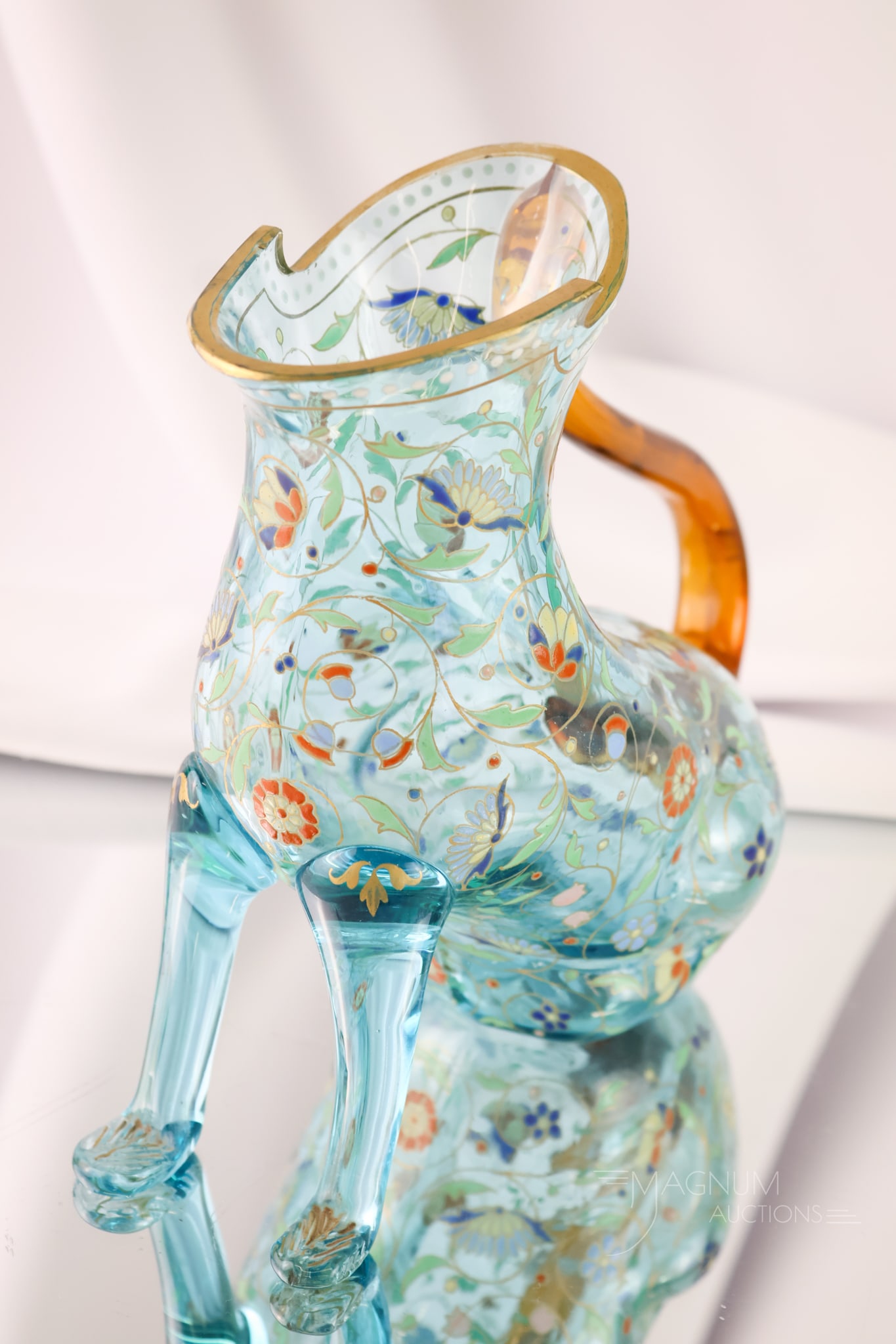 Moser Cat-Form Uranium Enamel Decorated Art Glass Pitcher: An unusual find in a Moser Cat-form art glass pitcher. This one is in uranium-rich blue glass with enamel decoration and an amber handle. The pitcher measures 7 3/4" tall and 8" wide.