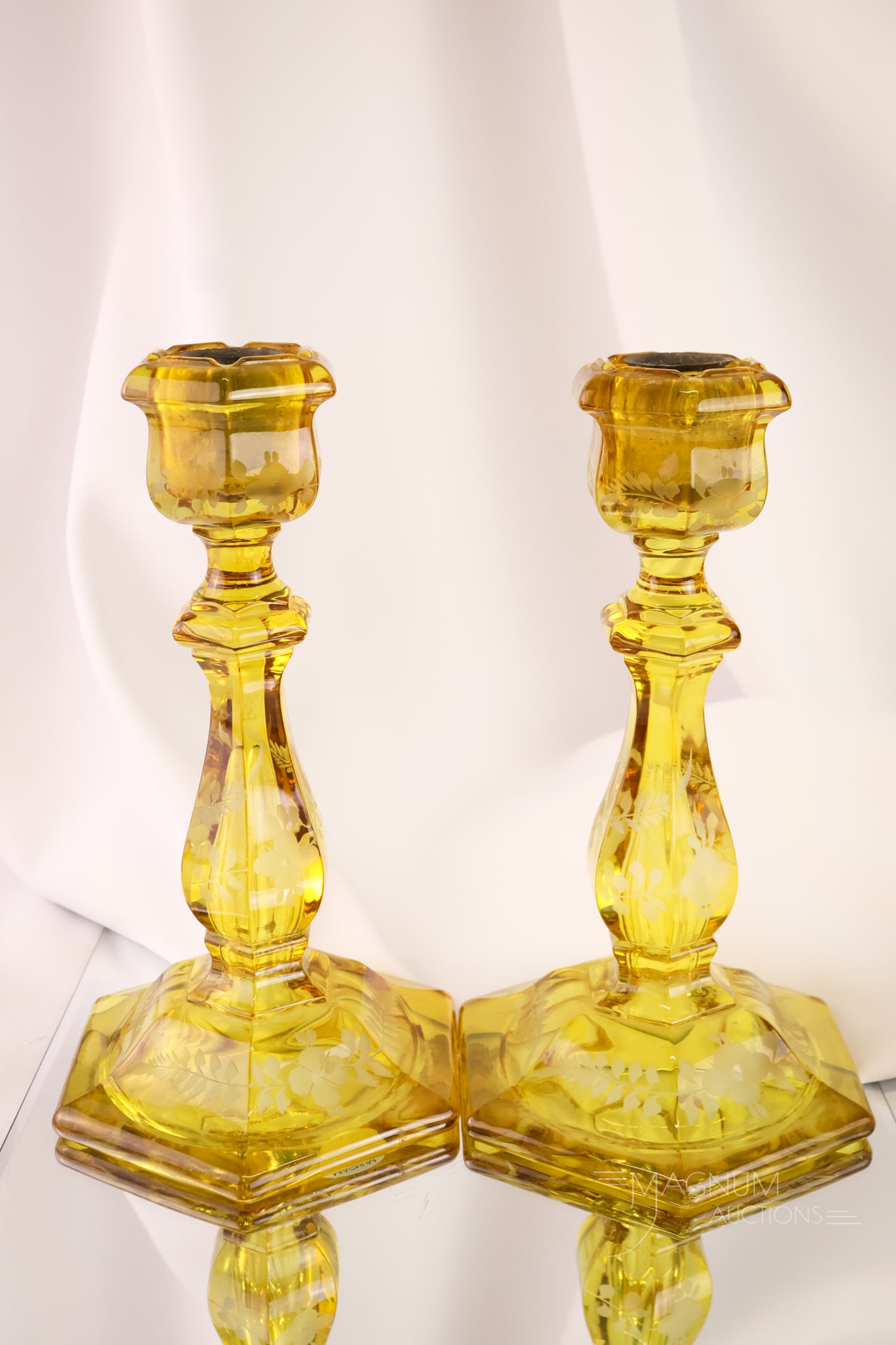 Pair 1930s Amber Stained Engraved Glass 10" Candlesticks: A select offering of a pair of amber-stained engraved glass candlesticks. Each is in golden amber. The candlesticks are engraved. They measure 10" tall and 6" wide.