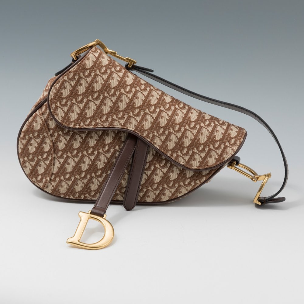 DIOR.  Saddle bag. Exterior in fabric with brown logo and short handle in dark brown leather. Gold (1 of 5)