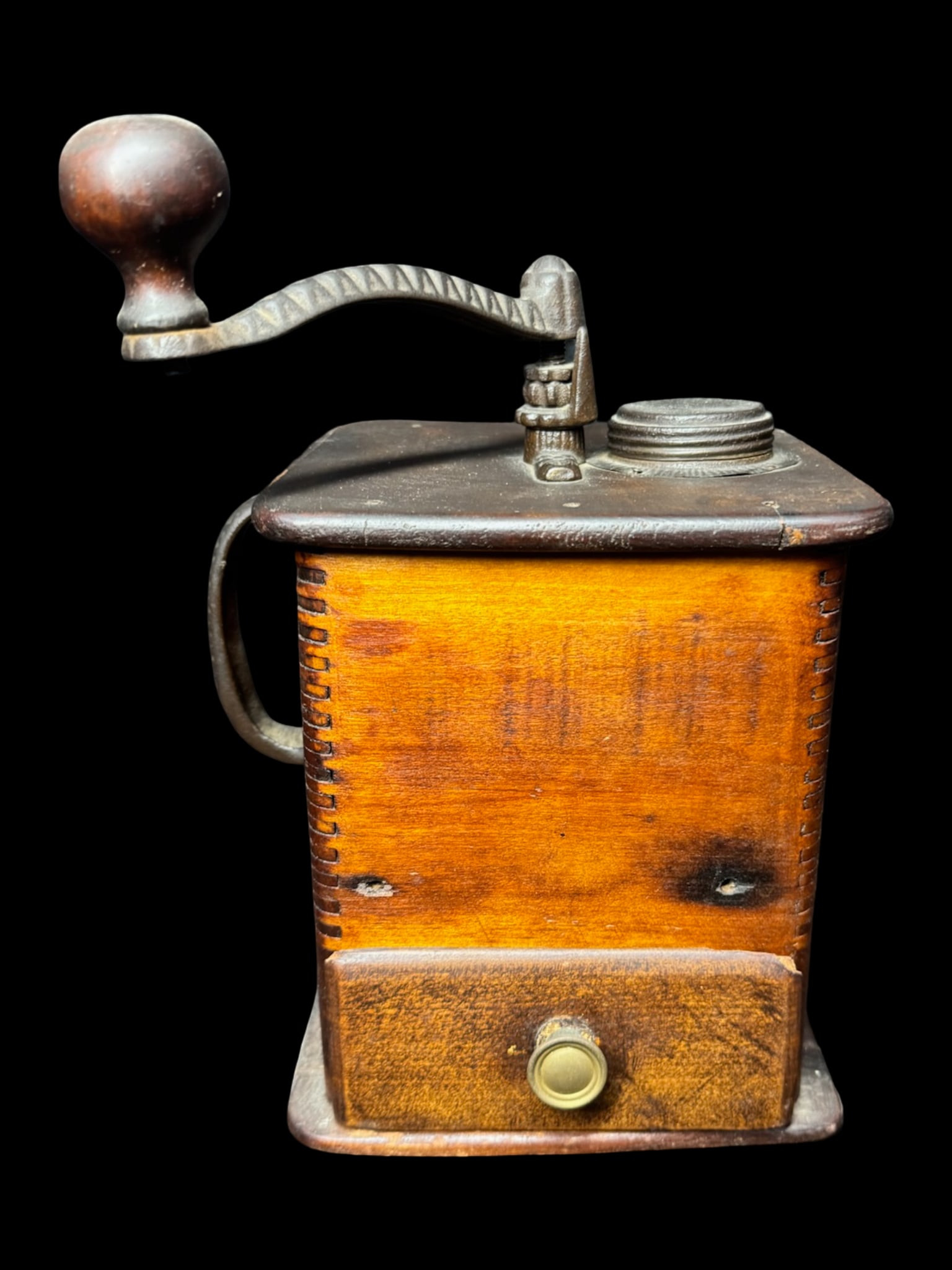 Antique Late Nineteenth Century Box Coffee Grinder: This antique coffee grinder has classic dovetailed wood construction, or box joints. It features an iron crank system with a rounded wooden turning knob, and a distinct cast iron loop handle. There is
