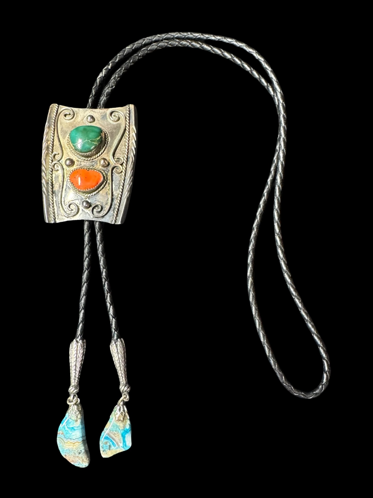 Sterling Silver Vintage Southwest Bolo Tie: This striking sterling silver bolo tie balances rugged frontier tradition with artisan silversmithing. The sterling silver slide features green turquoise and red coral, framed by scrollwork and beads.