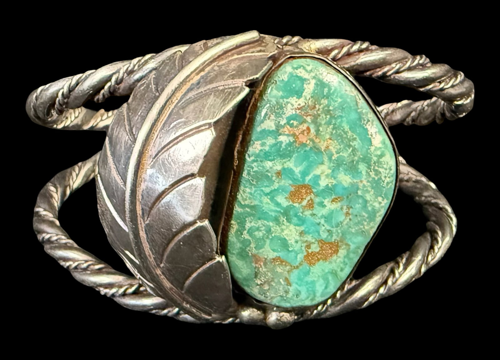 Sterling Silver Navajo Split Shank Turquoise Cuff: This Navajo sterling silver cuff bracelet features a large green-blue hand-cut matrix-rich stone, mounted in a smooth bezel. On one side there is a detailed hand-carved silver feather or leaf. The