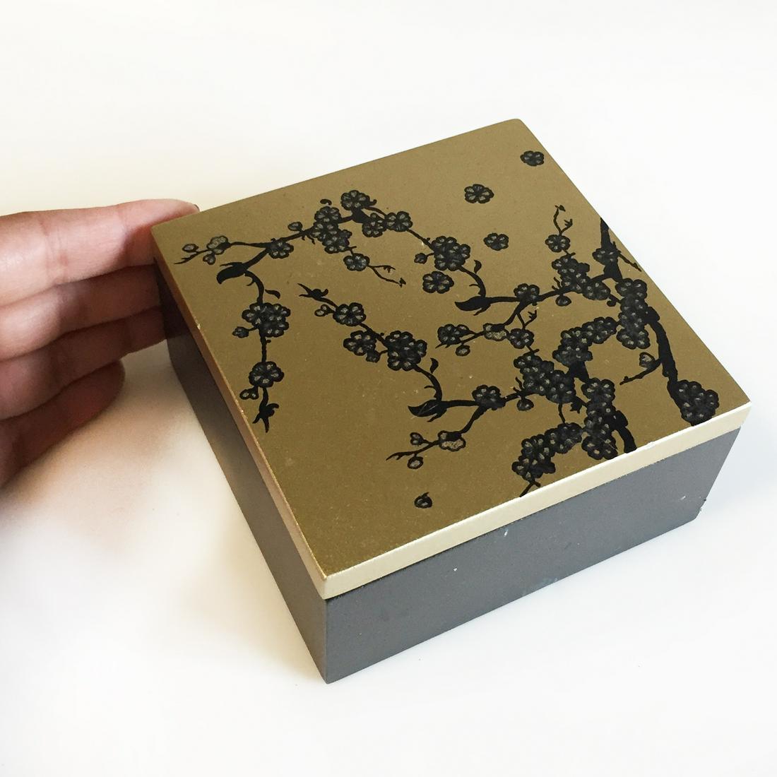 Black and gold painted flower on lid square jewelry box: Black and gold painted flower on lid square jewelry box. Measured 4 1/8 x 4 1/8 x 2 inches. Box has slots for rings and 2 compartments for other jewelry. Condition good.