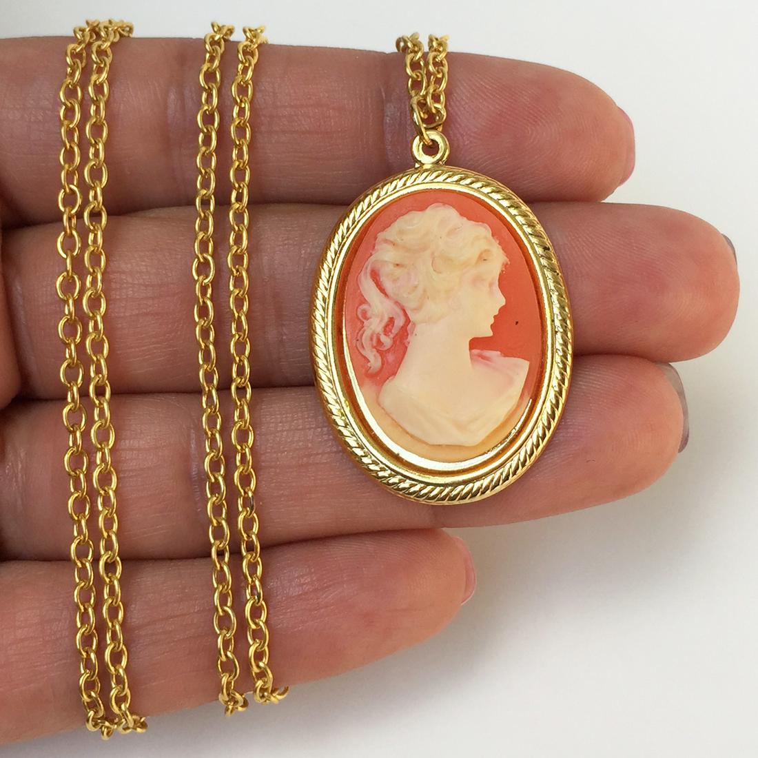Gold tone Cameo pendant and chain necklace: Gold tone woman's face Cameo on orange background pendant and chain necklace. Pendant length 1 1/2 inches with bail. Chain length 30 inches. Condition very good.