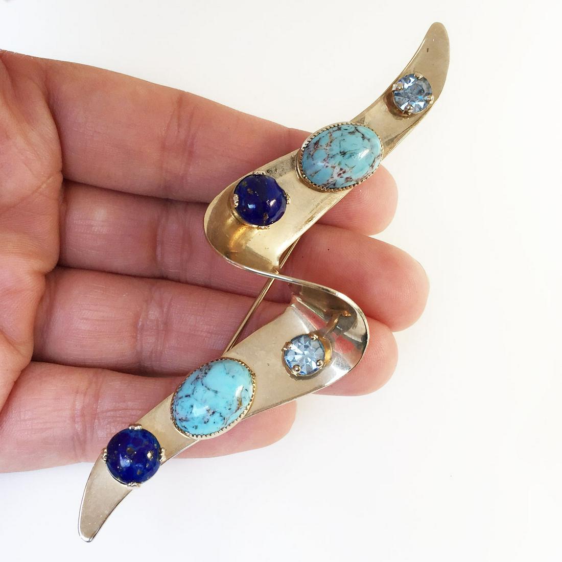 Vtg gold tone turquoise color lapis color cab brooch: Vintage gold tone blue crystals, oval turquoise color, round lapis color cabochon Ribbon Wave shape brooch. Measured 4 x 1 1/2 inches. Condition very good.
