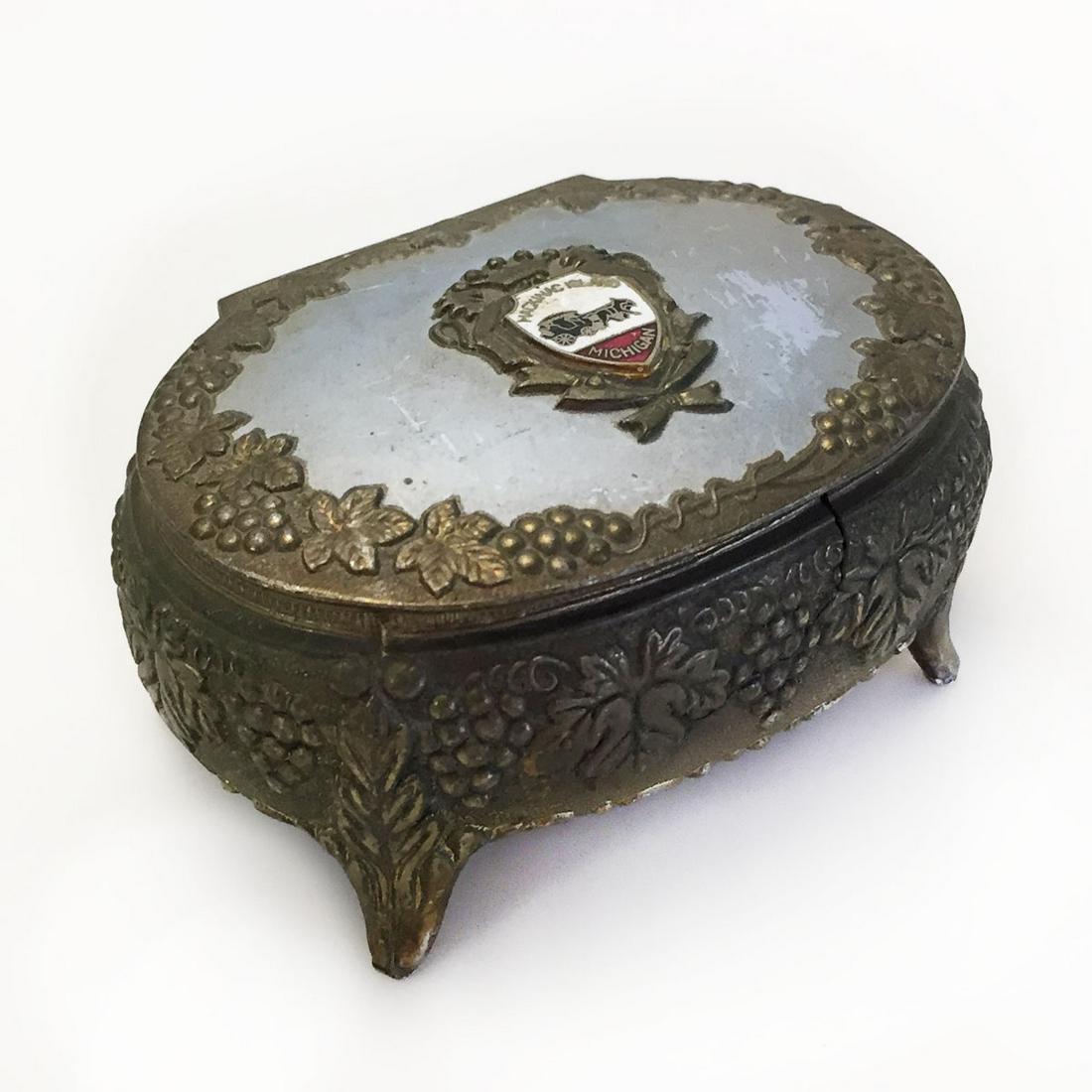 Bronze tone Grape cluster oval trinket jewelry box: Bronze tone gray top Grape Cluester Vines Leaves relief accent and Macking Island Michigan coat of arms oval shape trinket jewelry box with legs Japan. Box measured 3 1/4 x 2 1/8 x 1 3/4 inches with l