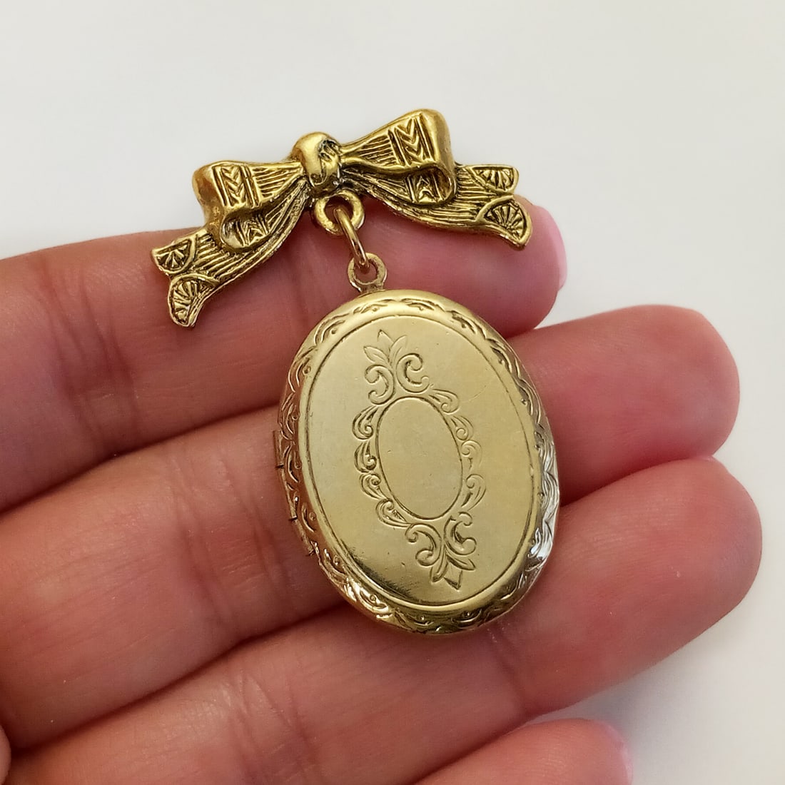 Gold tone Ribbon and oval locket brooch: Gold tone textured finish Ribbon and oval locket brooch. Measured 1 5/8 x 1 1/4 inches. Condition very good.