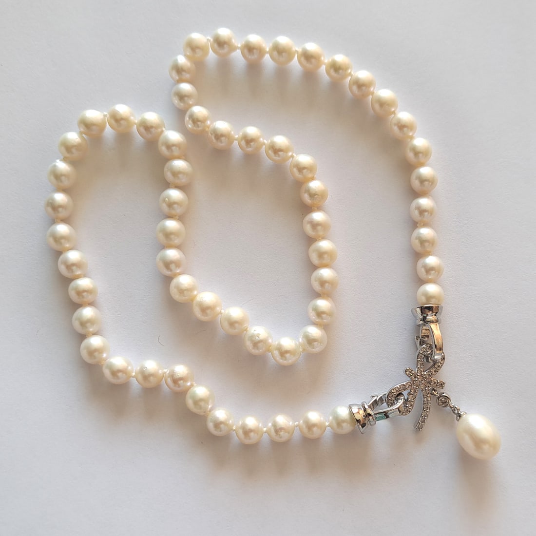 6.5-7 mm South Sea white almost round knotted pearl necklace with silver tone and CZ bow clasp: 6.5-7 mm South Sea white almost round knotted pearl necklace with silver tone and CZ bow clasp pendant with enchancers. Length 18 inches. Pearls measured 6.5-7 mm in diamter, have clean skin and high 