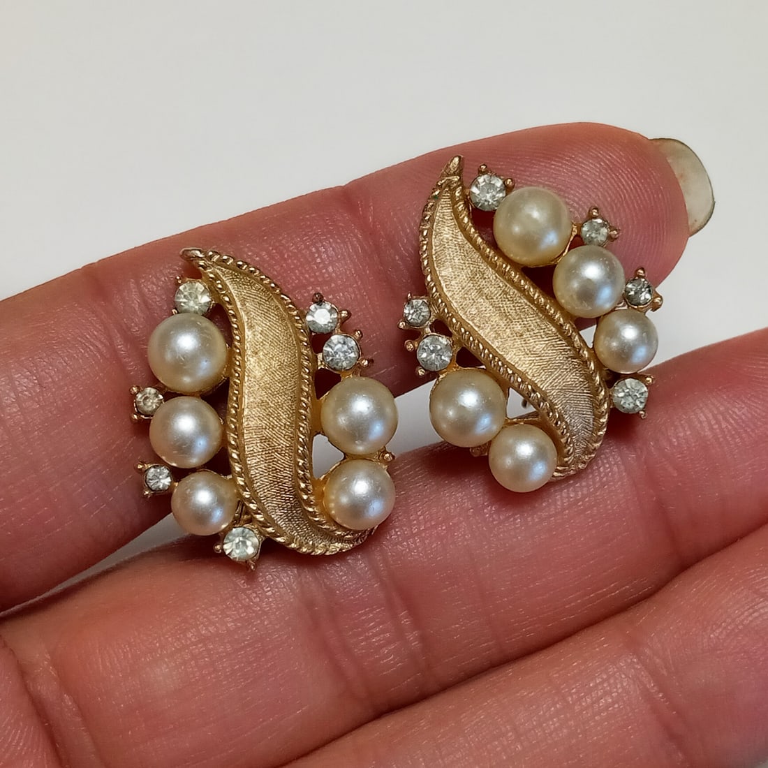 TRIFARI Vintage gold tone faux pearl and clear rhinestones ear clips, signed: TRIFARI Vintage gold tone textured finish, white faux pearl and clear rhinestones ear clips, signed. Length 7/8 inches. Hallmarked Trifari, copyright symbol. Condition very good.