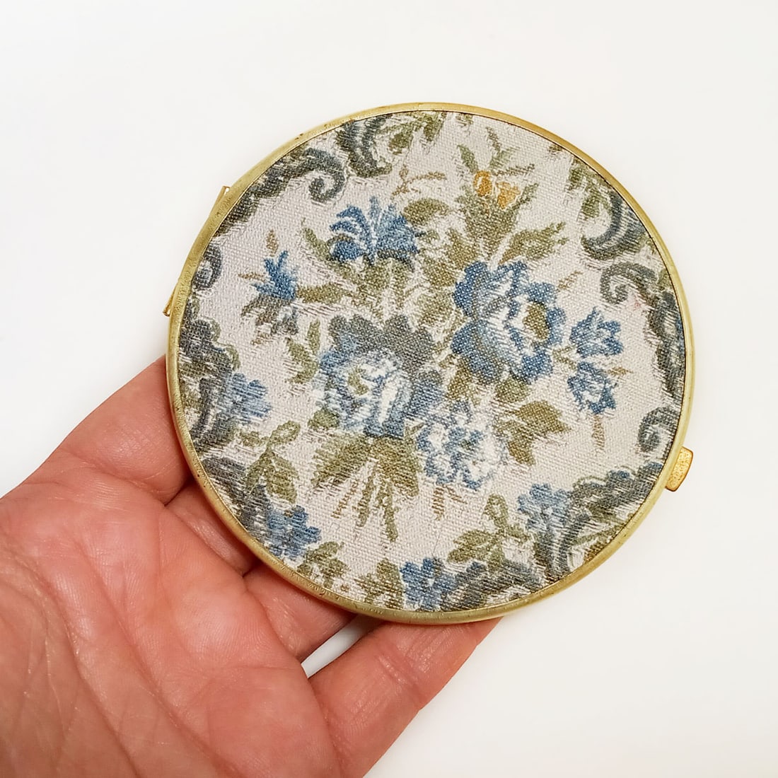 Gold tone blue Flowers fabric look mirror compact: Gold tone blue Flowers textured fabric look round double mirror compact. Measured 3 1/2 inches in diameter. Has two mirrors: one regular, one with magnification. Looks like fabric but material is more
