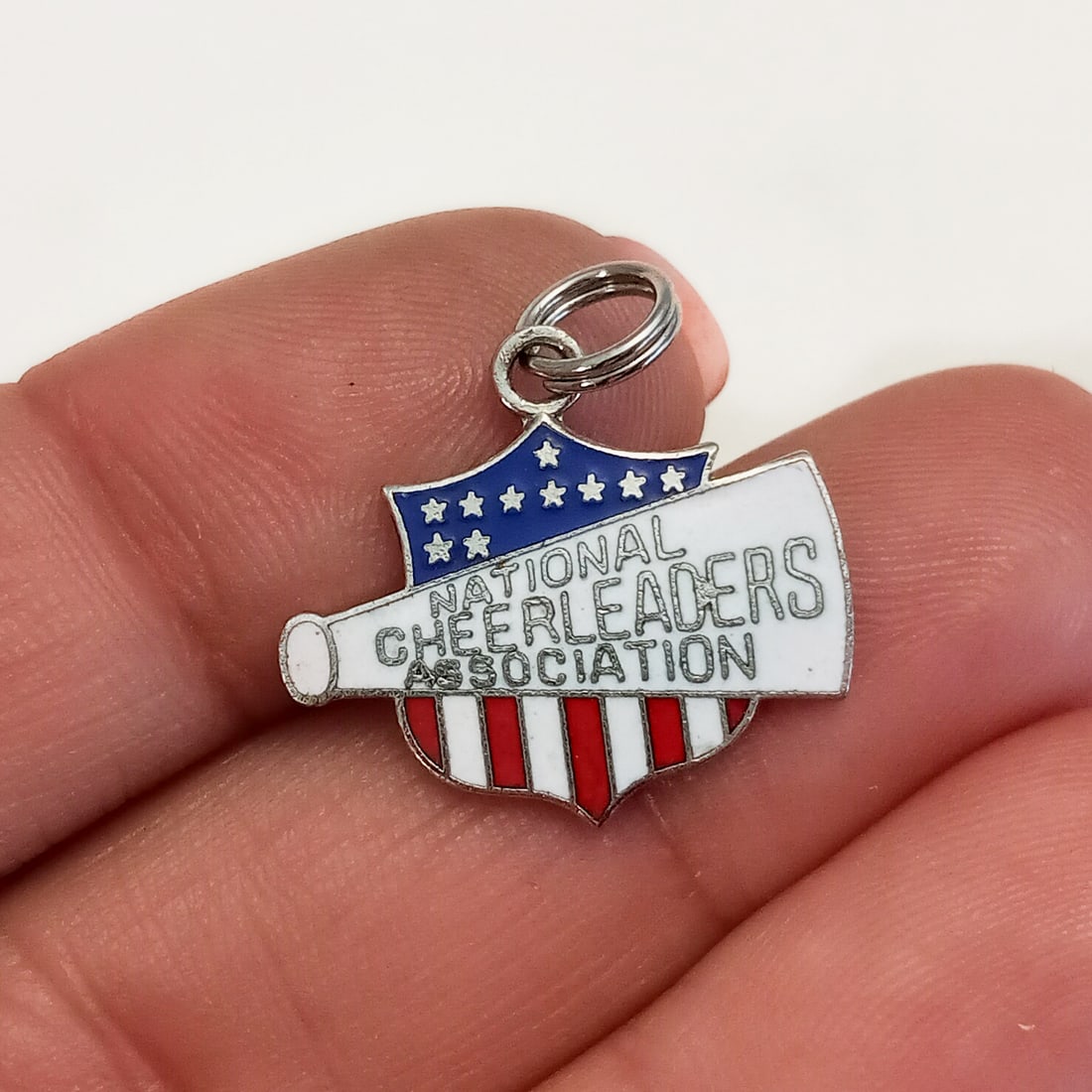 Silver tone National Cheerleaders Association charm: Silver tone red, white and blue National Cheerleaders Association charm. Length 3/4 inches with bail. Hallmarked NCA, Box 30175 Dallas, Texas. Condition very good.