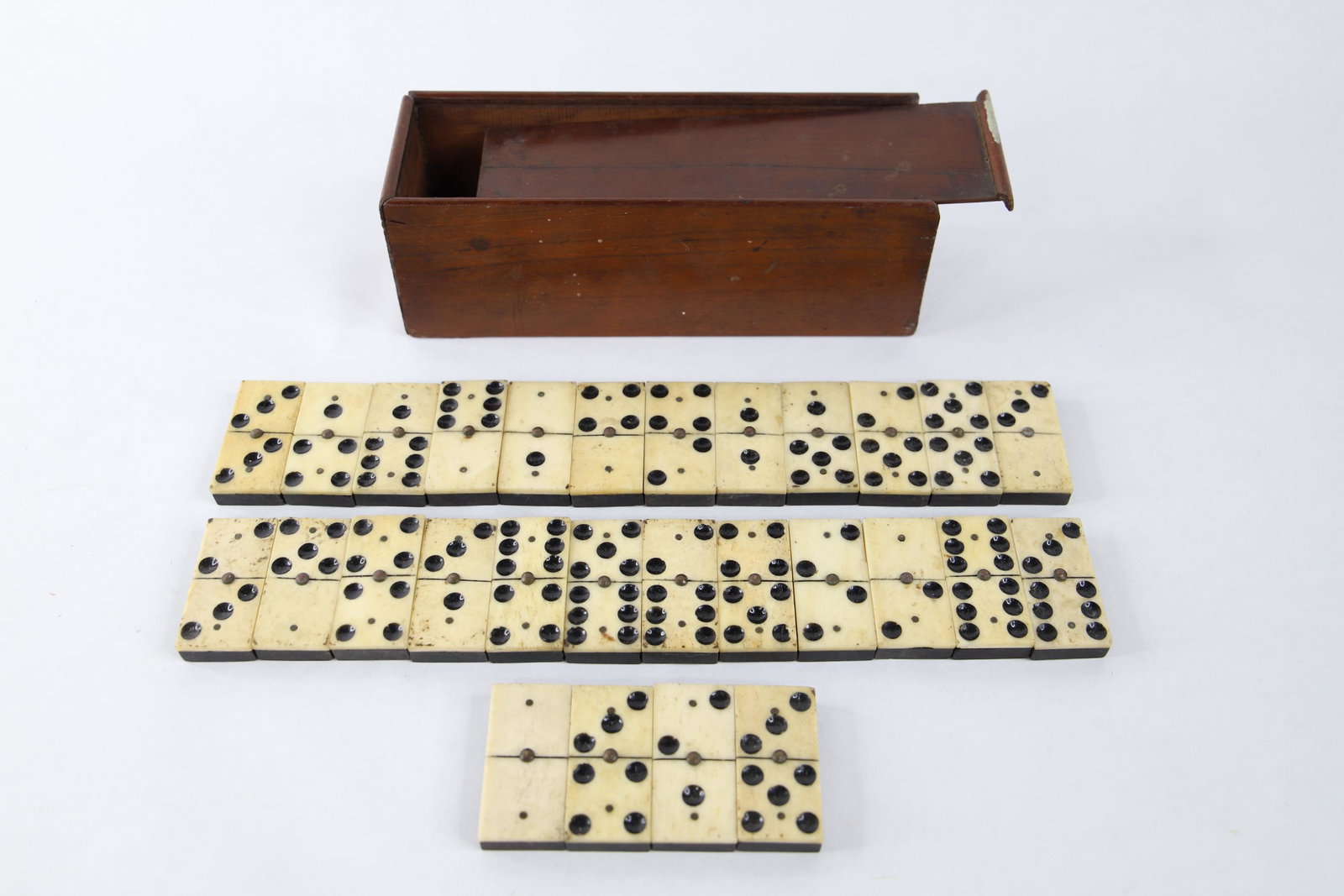 Bone Ebony Domino Set: Twenty-eight piece domino set made of bone and ebony; Wood box has brass nails; No visible maker's mark; Box measures approximately H 2 1/4 x W 7 x D 2 1/4 inches; Dominoes measure approximately H 1/4